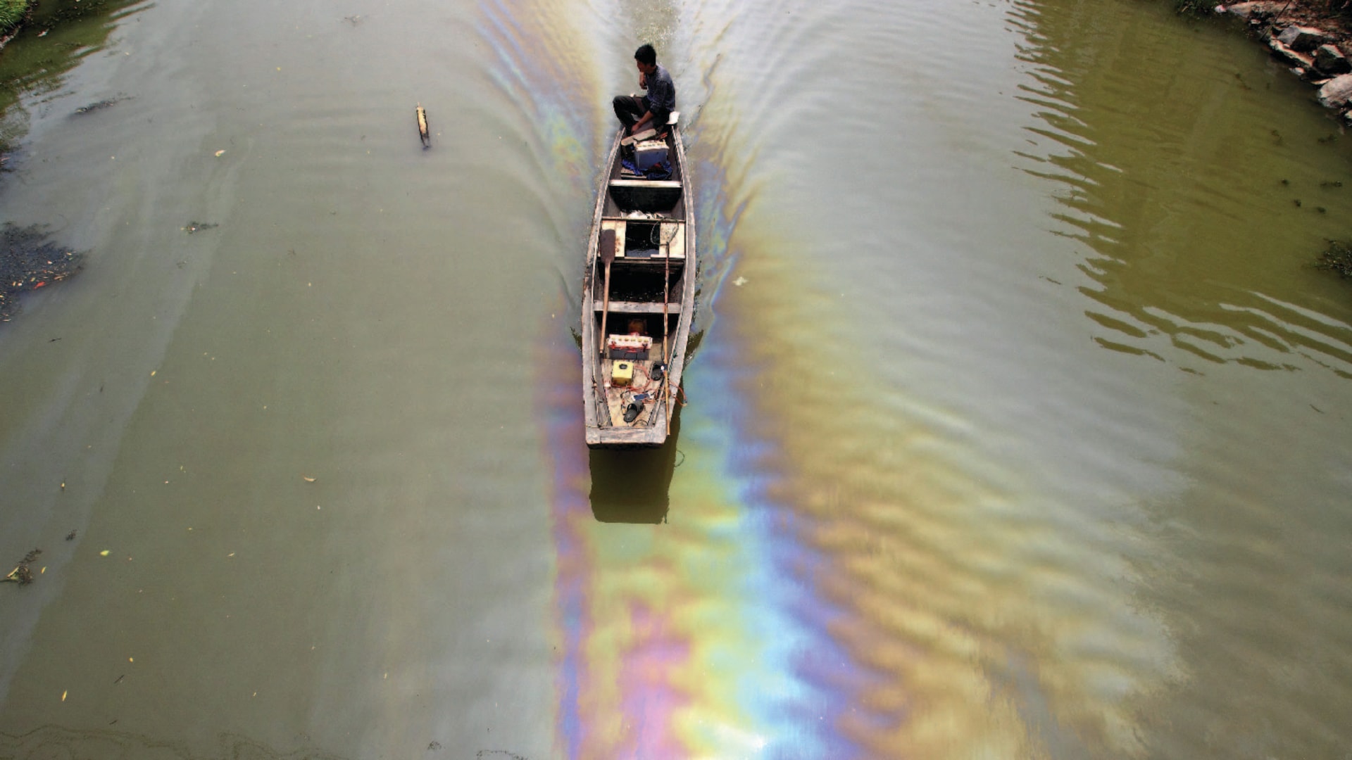 A man drives a boat along a river polluted by leaked fuel, in Shaoxing, China.
