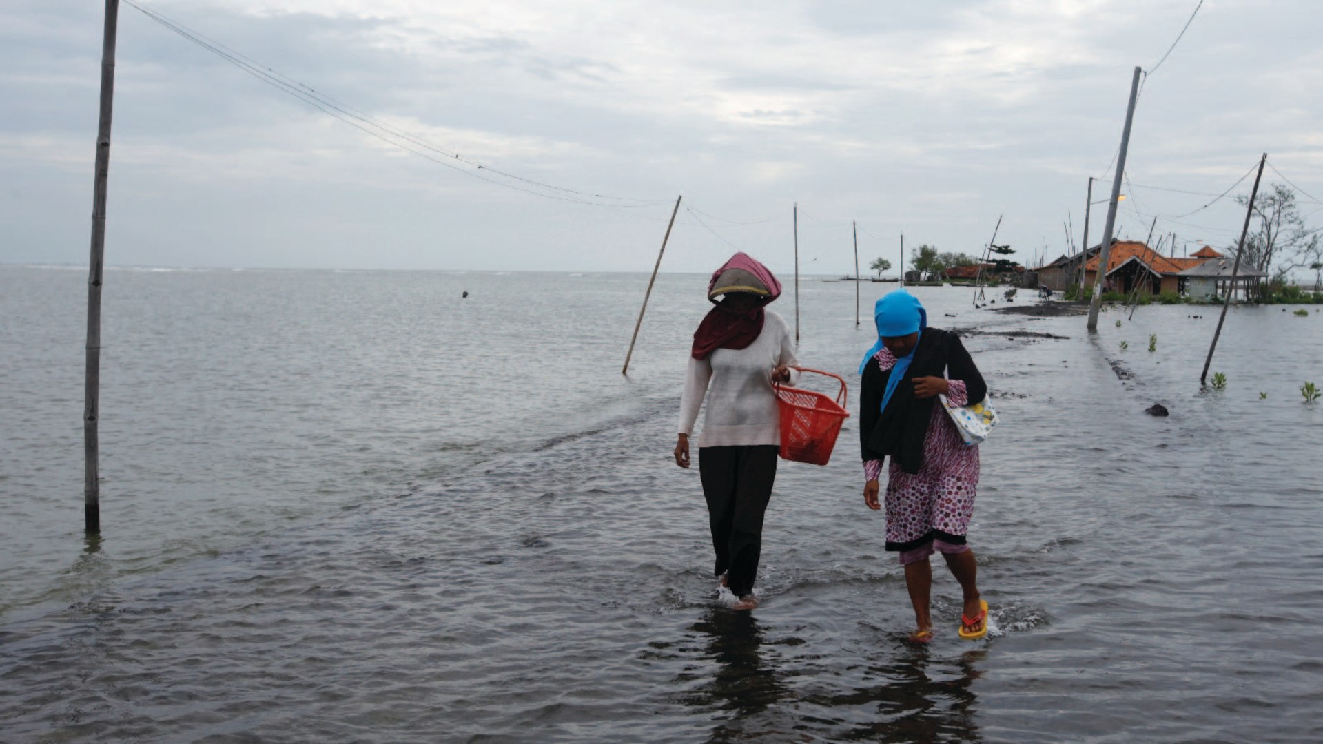 Villagers walk along a street flooded with sea water in Subang, Indonesia