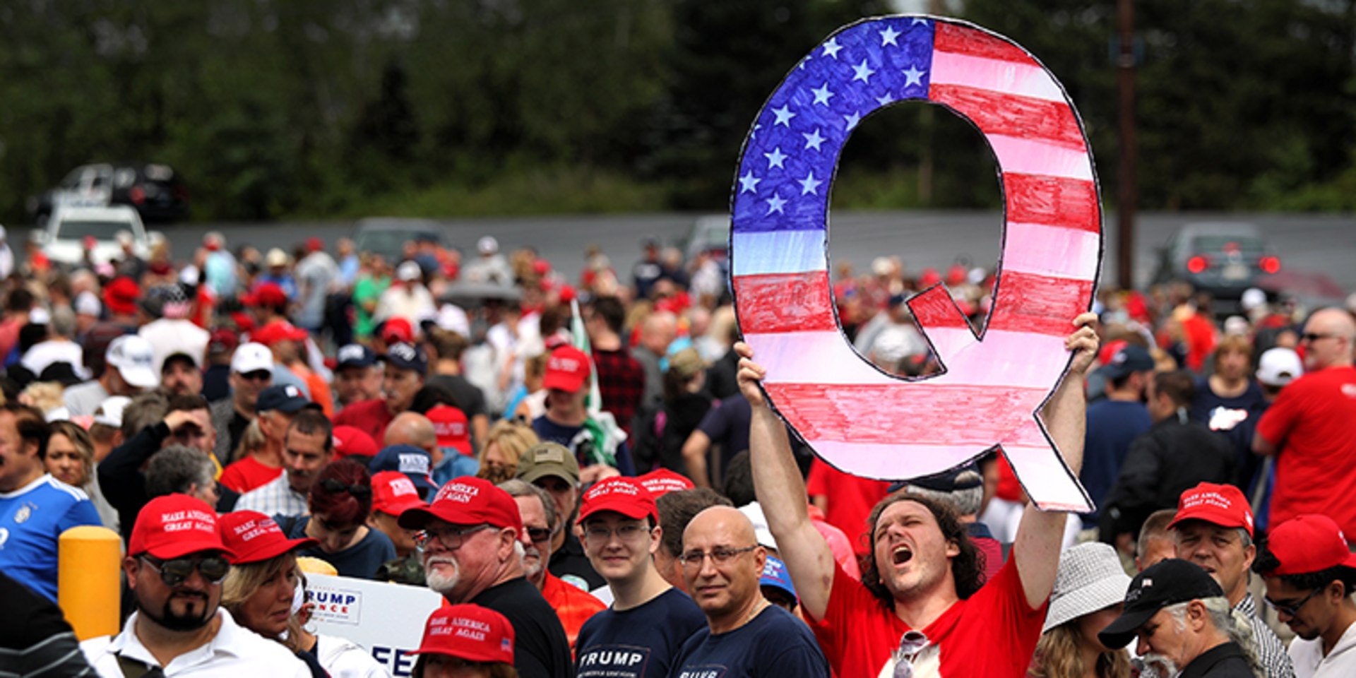 A man holds up a large ”Q” sign while waiting in line to see then-President Donald J. Trump at his rally on August 2, 2018, in Wilkes Barre, Pennsylvania. ”Q” represents QAnon, a conspiracy theory group.