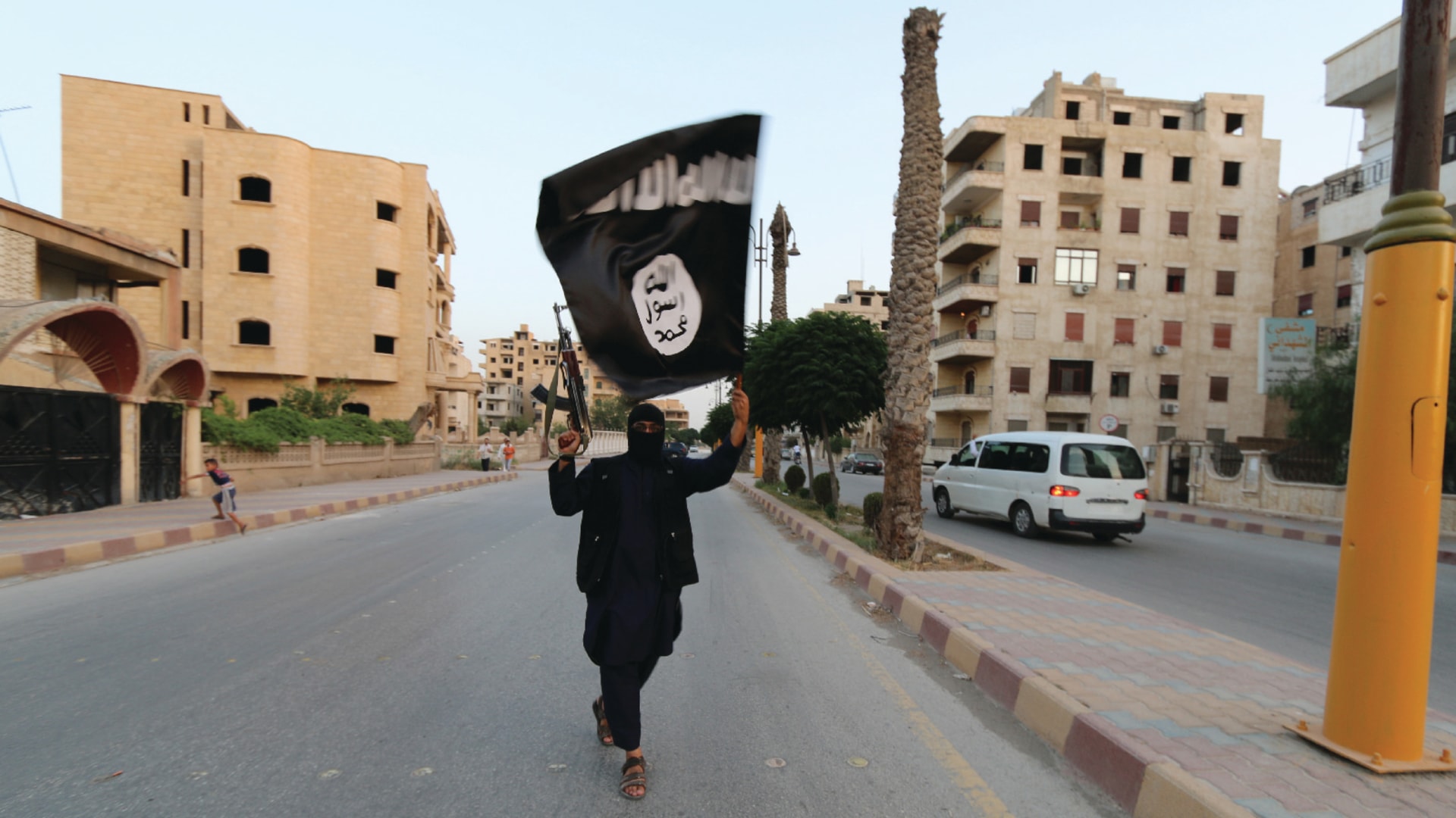 A member loyal to the Islamic State holds a gun and waves an ISIS flag in Raqqa, Syria.