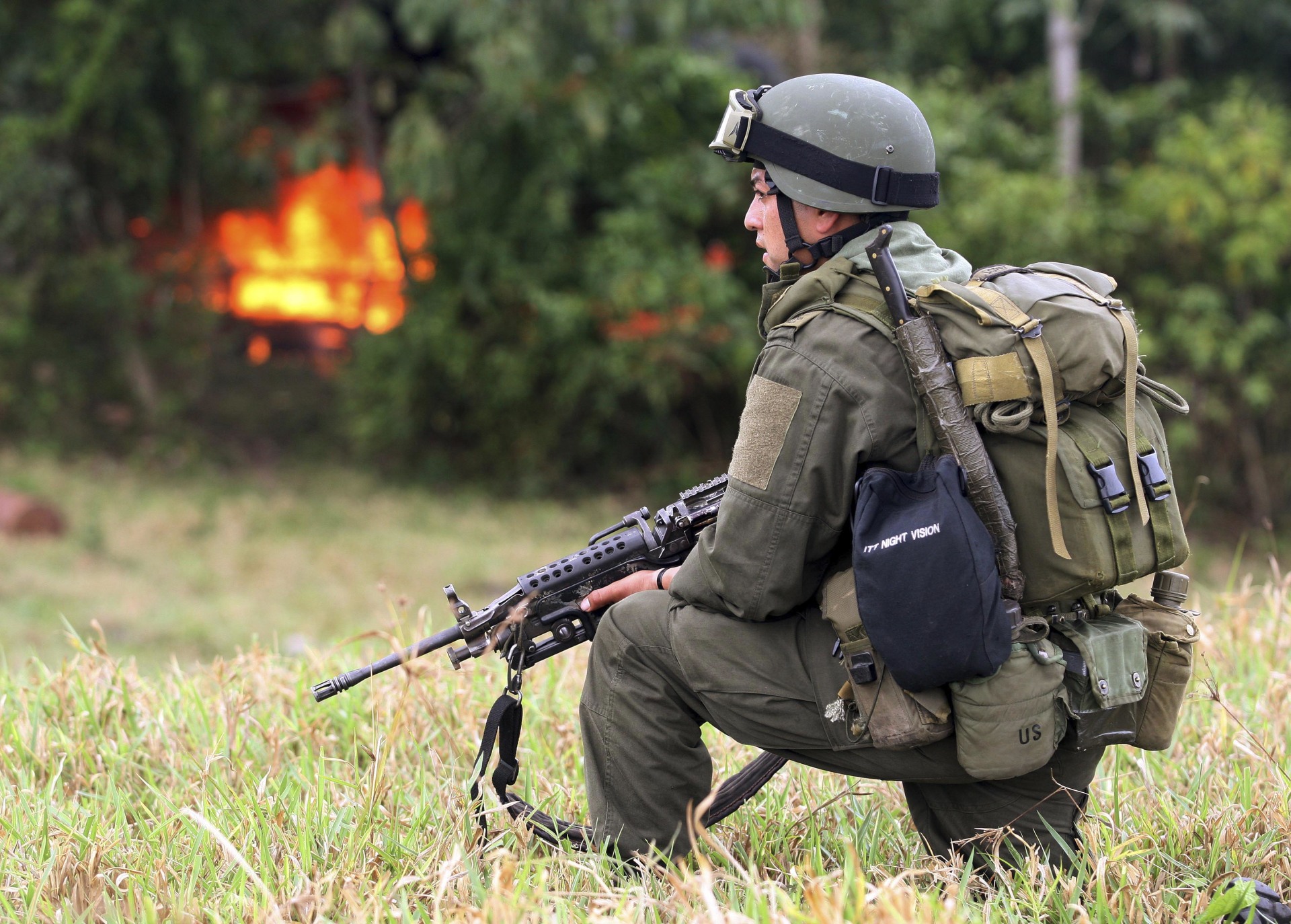 A Colombian anti-drug police officer stands guard after burning a cocaine laboratory, which is seen in the background.