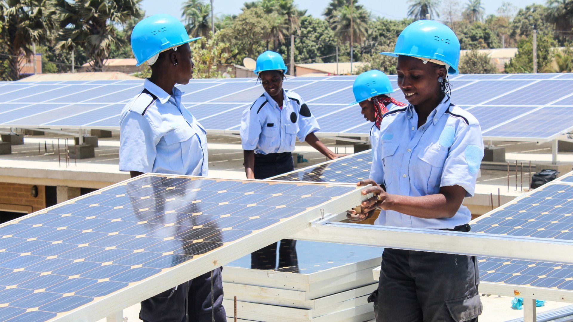 Young women, wearing blue helmets, trained at the Fandema Center install solar panels and train their peers in Tujeren, Gambia.