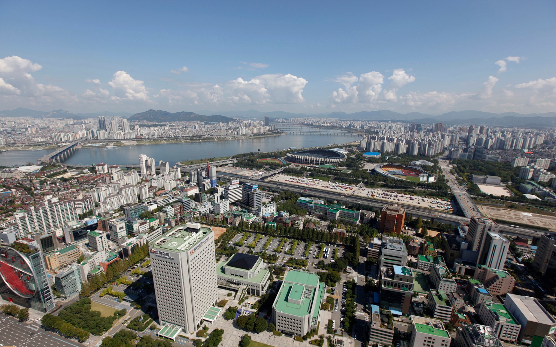Many modern buildings and skyscrapers stretch along a river all the way to the mountains on the horizon.