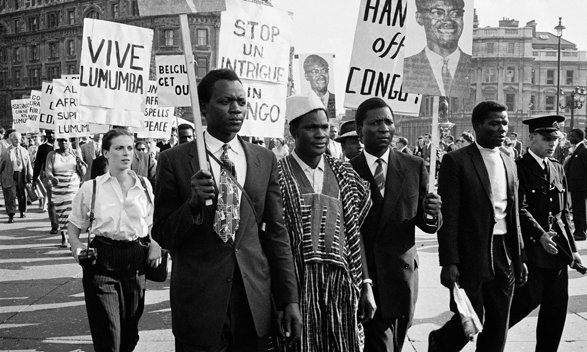 Black and white photo of Black and white protesters marching with signs reading ”Vive Lumumba” and ”Hands off Congo.”