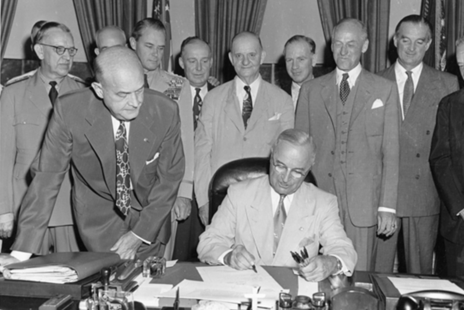 President Harry S. Truman is signing the National Security Act Amendment of 1949 in the Oval Office.