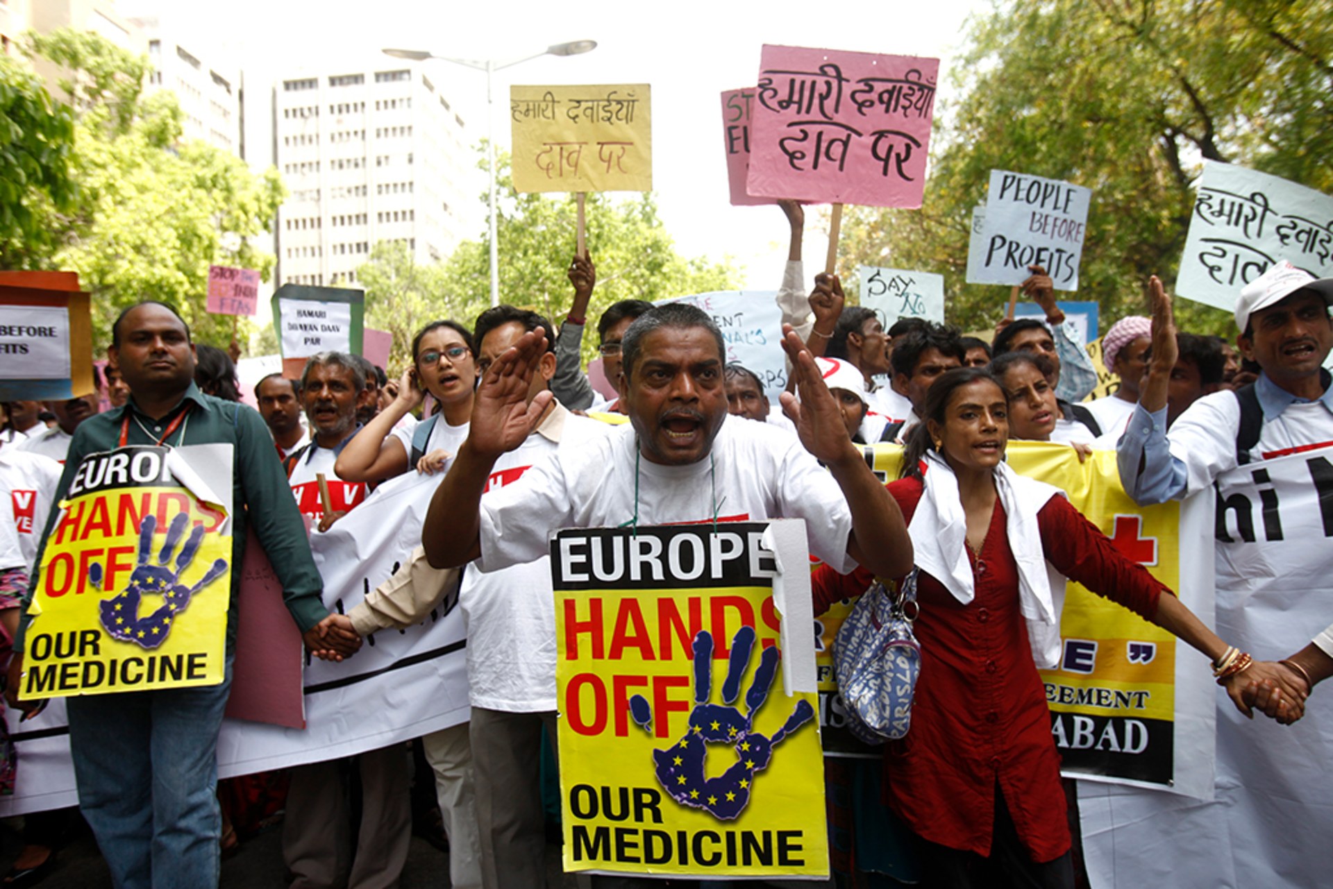 Indian demonstrators hold signs protesting a potential free trade agreement between the EU and India. The man in front wears a sign around his neck that reads, "Europe, hands off our medicine."