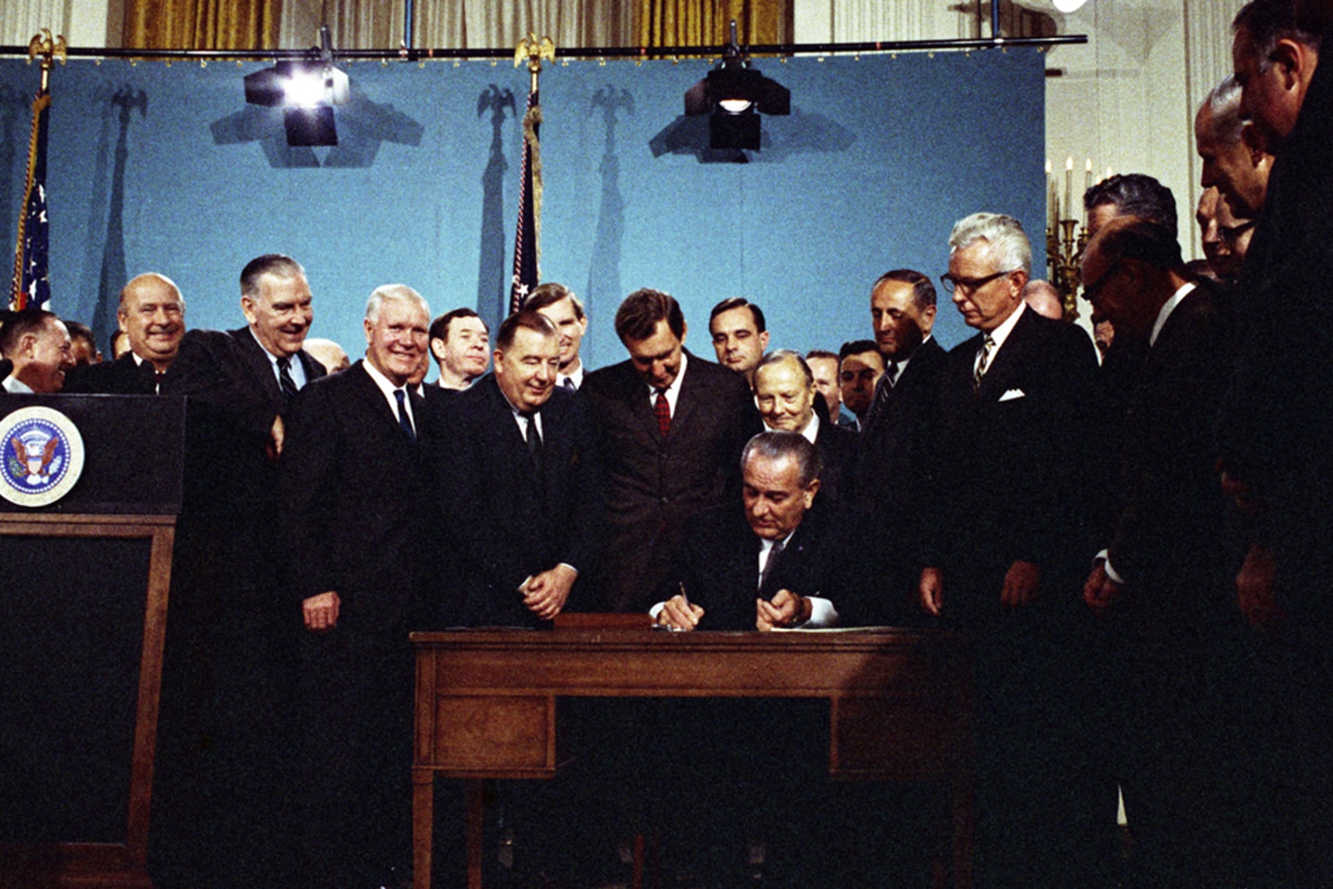 President Lyndon B. Johnson signs the Air Quality Act on November 21, 1967, as various men stand behind and around him.