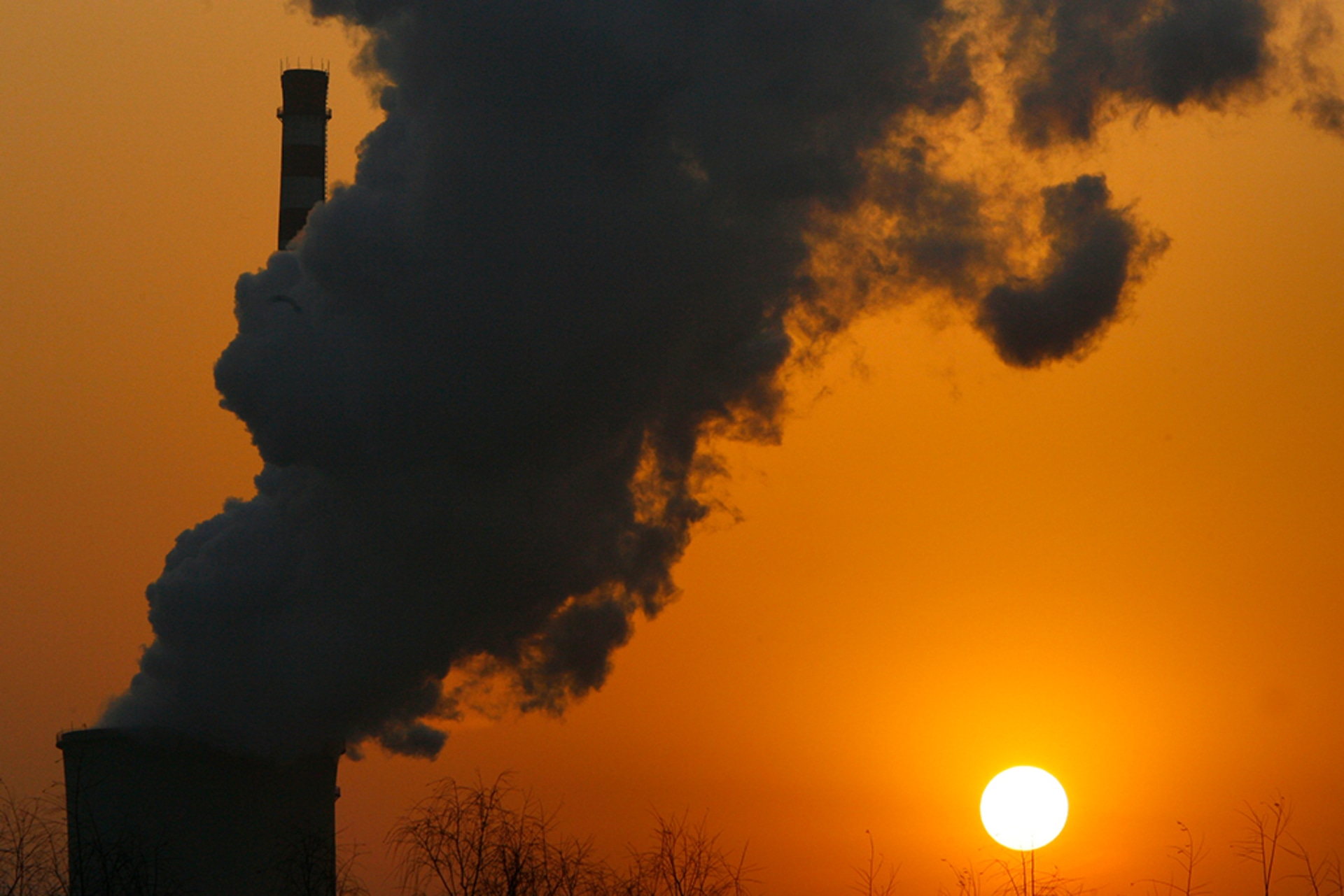 A sunset next to a coal-burning power plant as fumes rise from the top.