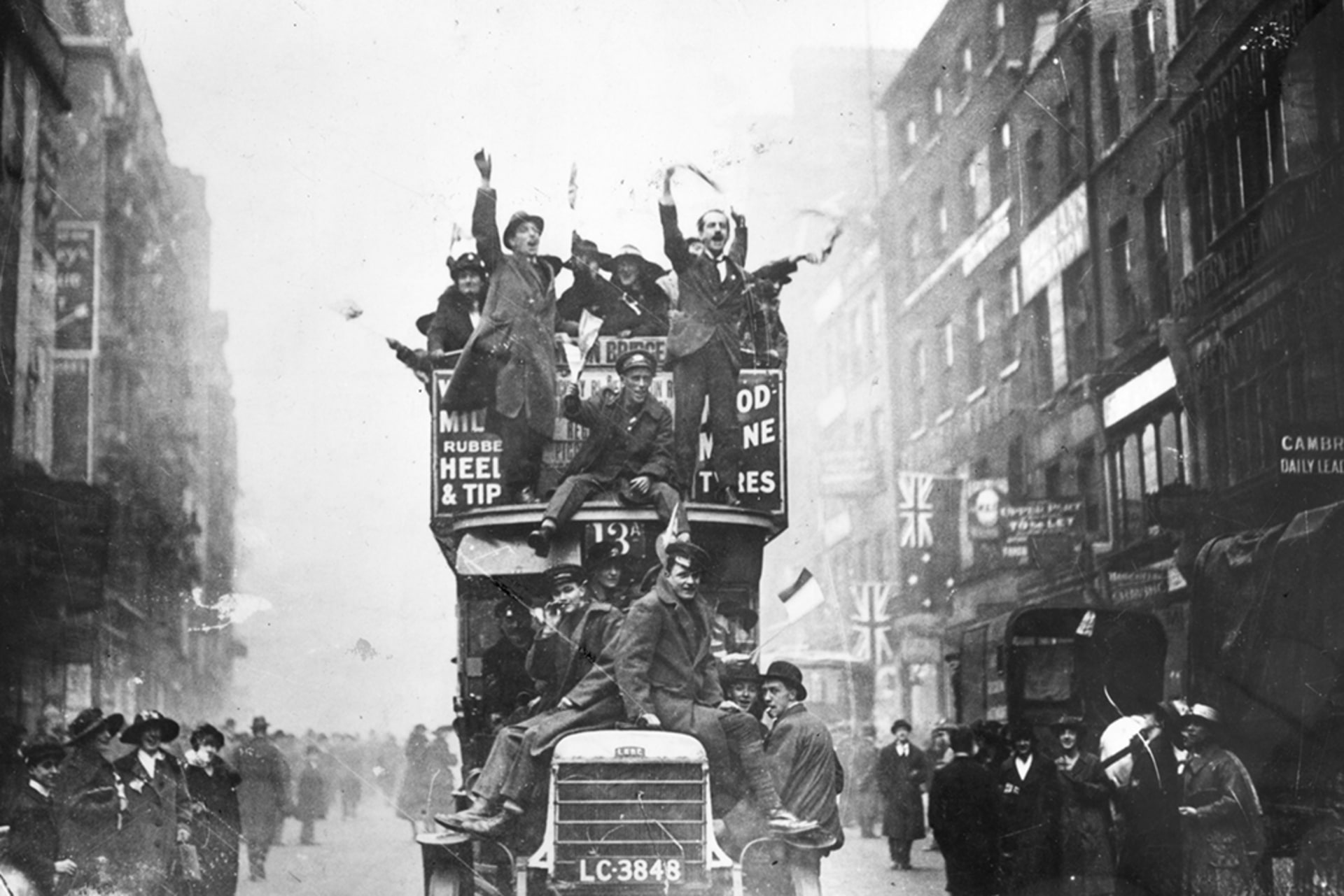 People on a vehicle raise their hands in celebration of Armistice Day as the car drives down the street.
