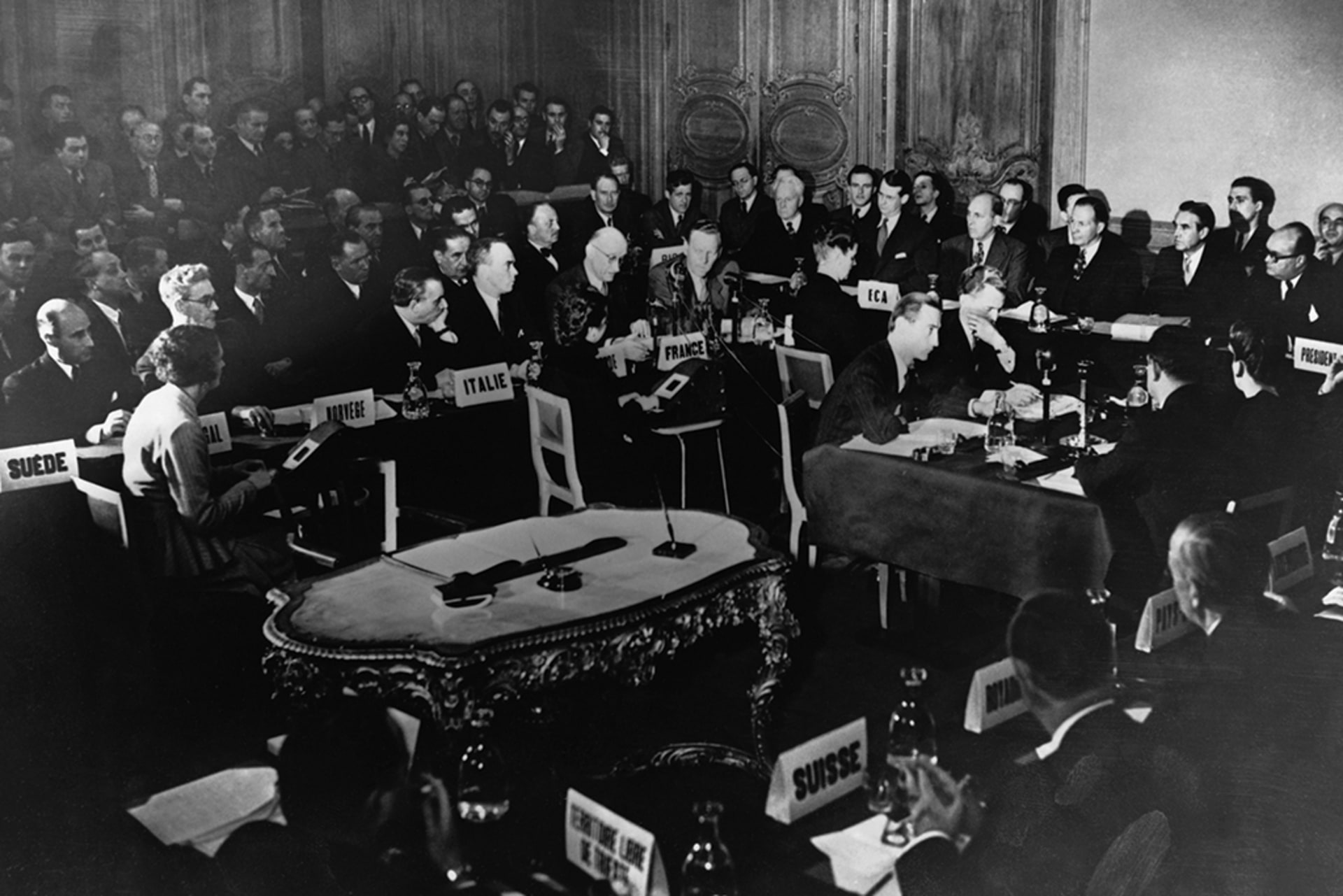 Many people seated a various tables discussing the Marshall Plan.
