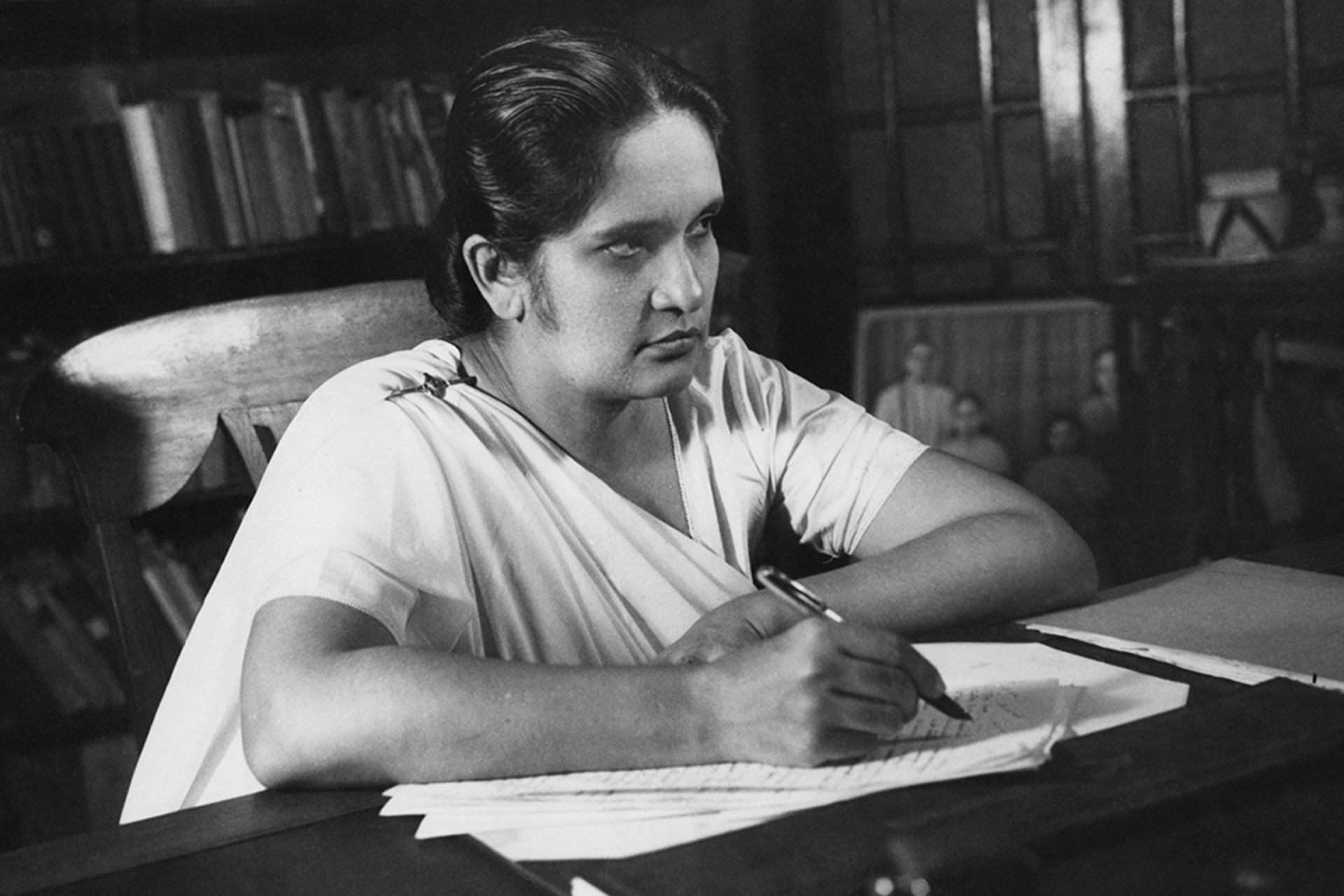 Sirimavo Bandaranaike writes at her desk while glancing up.