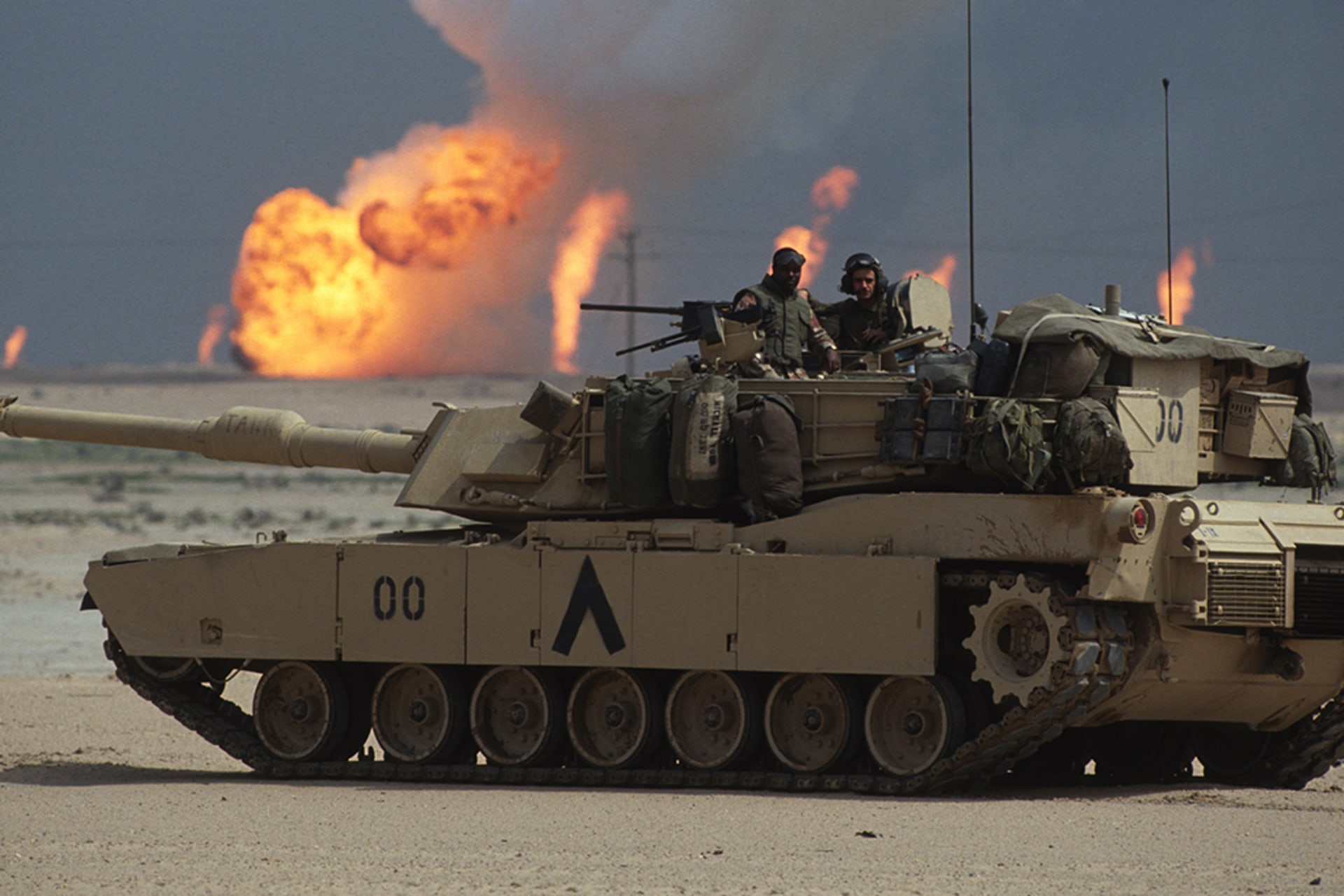 American soldiers standing in the turret of a tank in Kuwait as oil wells burn near the Iraqi border.