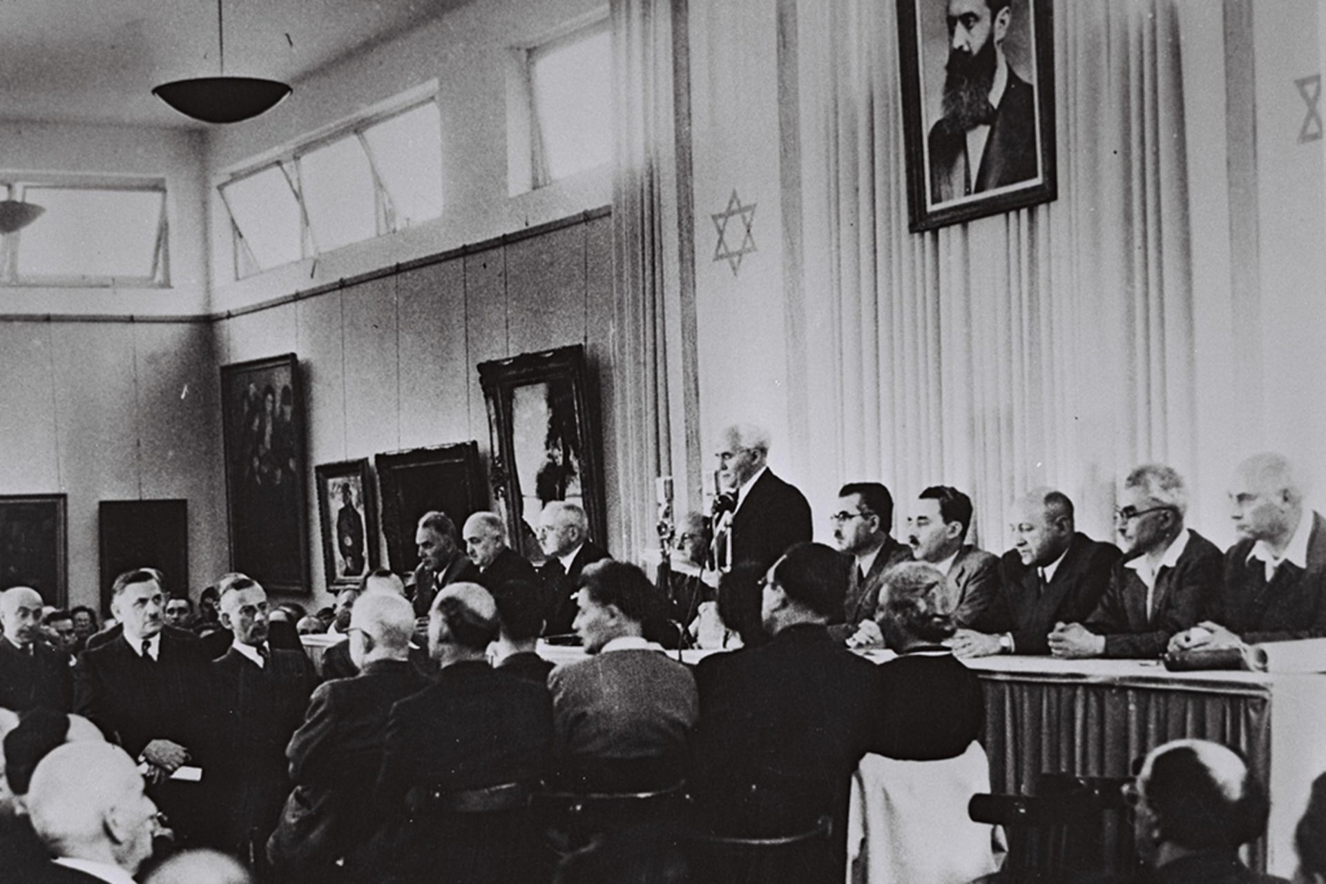 David Ben-Gurion, flanked by the members of his provisional government, reads the Declaration of Independence in the Tel Aviv Museum Hall.