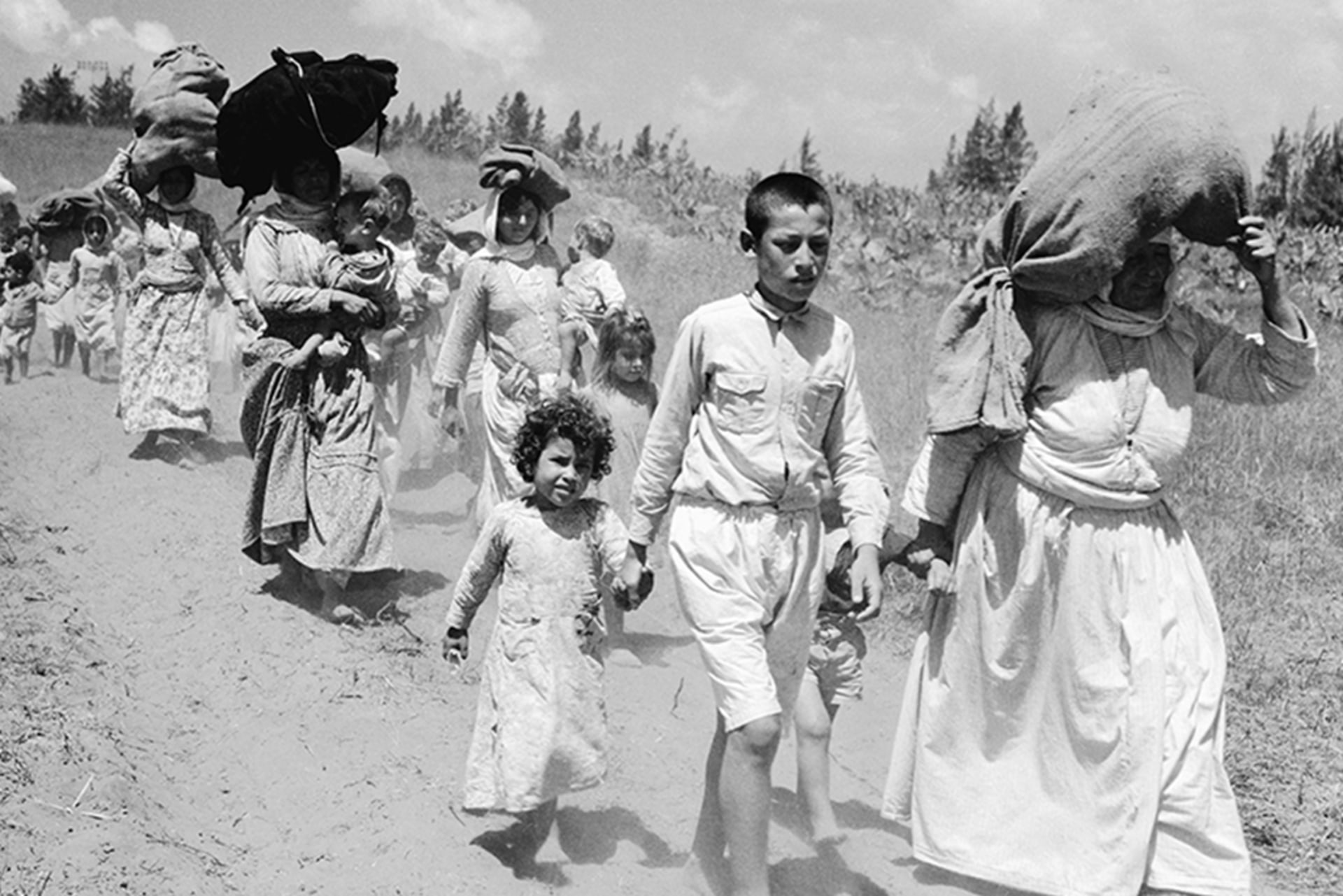 Palestinian women and children hike through the desert, some carrying large sacks with their belongings. The group heads toward Arab-controlled territory in the West Bank.