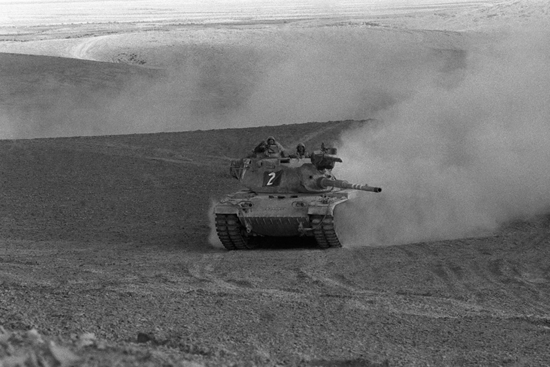 An Israeli tank in the Sinai Desert drives through the desert with a cloud of dust in its wake.