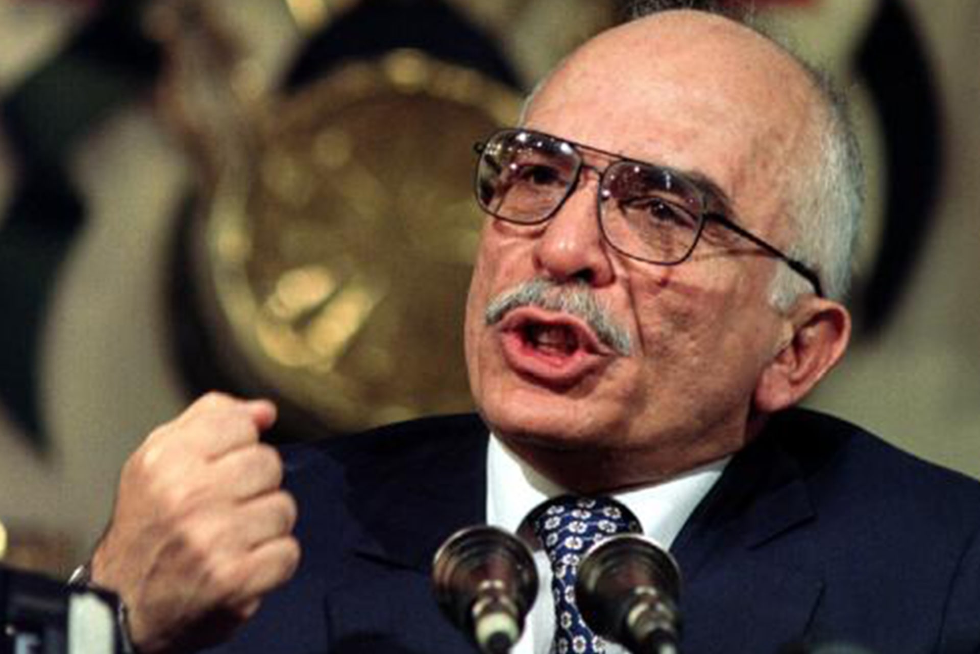 Jordan's King Hussein speaks passionately into a microphone with a clenched fist.