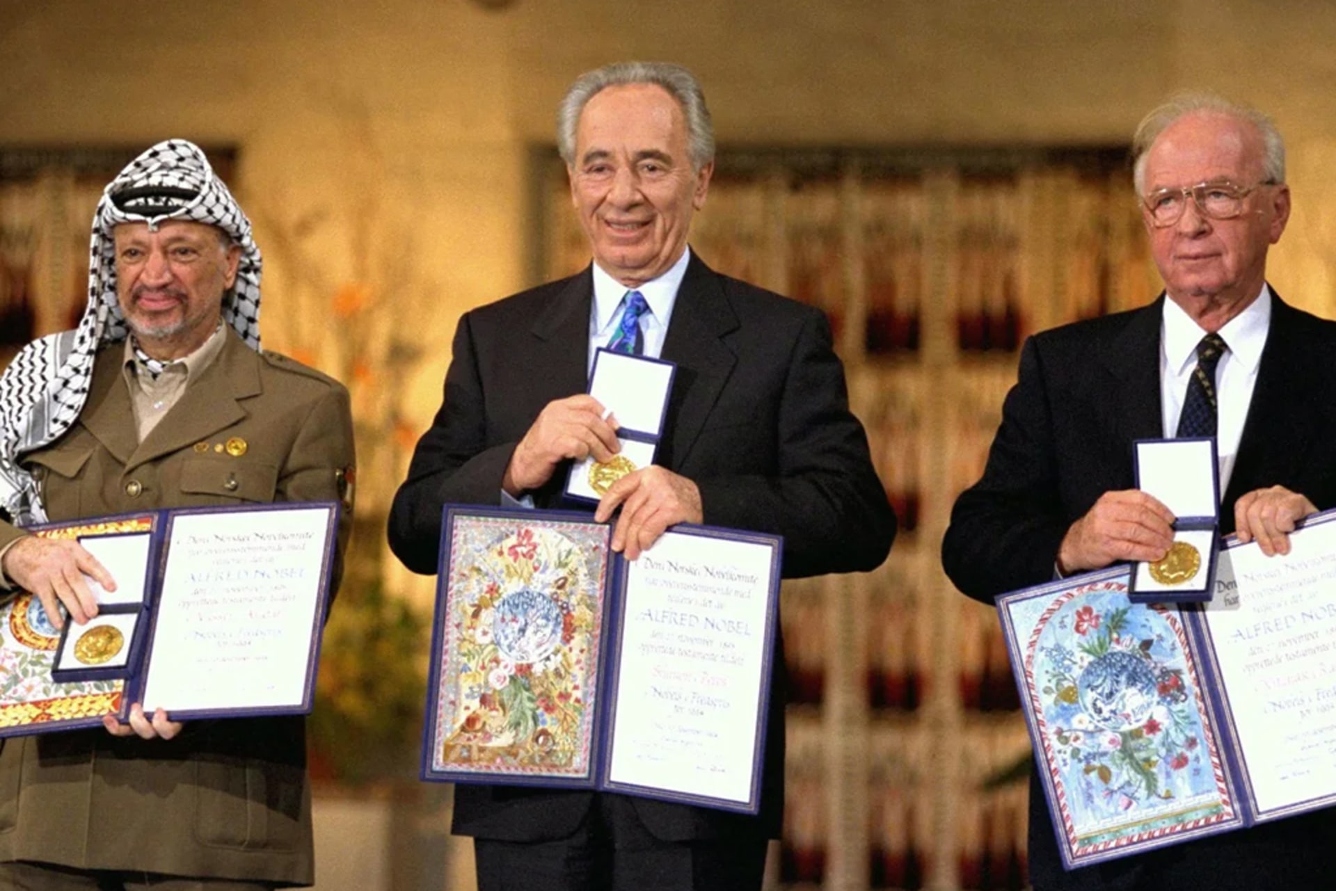 The Nobel Peace Prize Laureates for 1994 in Oslo, Prime Minister Yitzhak Rabin, Foreign Minister Shimon Peres, and PLO Chairman Yasser Arafat. The men are smiling together, each holding their prizes for the audience.