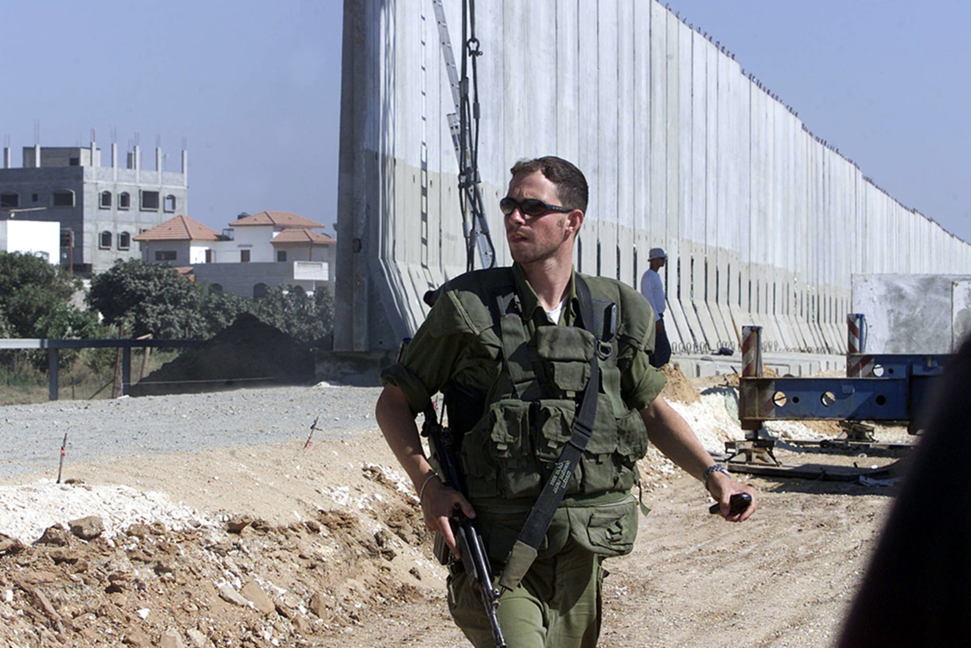 An Israeli soldier guards the working site of the new fence built by Israel on the outskirts of the Palestinian West Bank city. The soldier looks off to the side while holding his gun in the holster at his side.