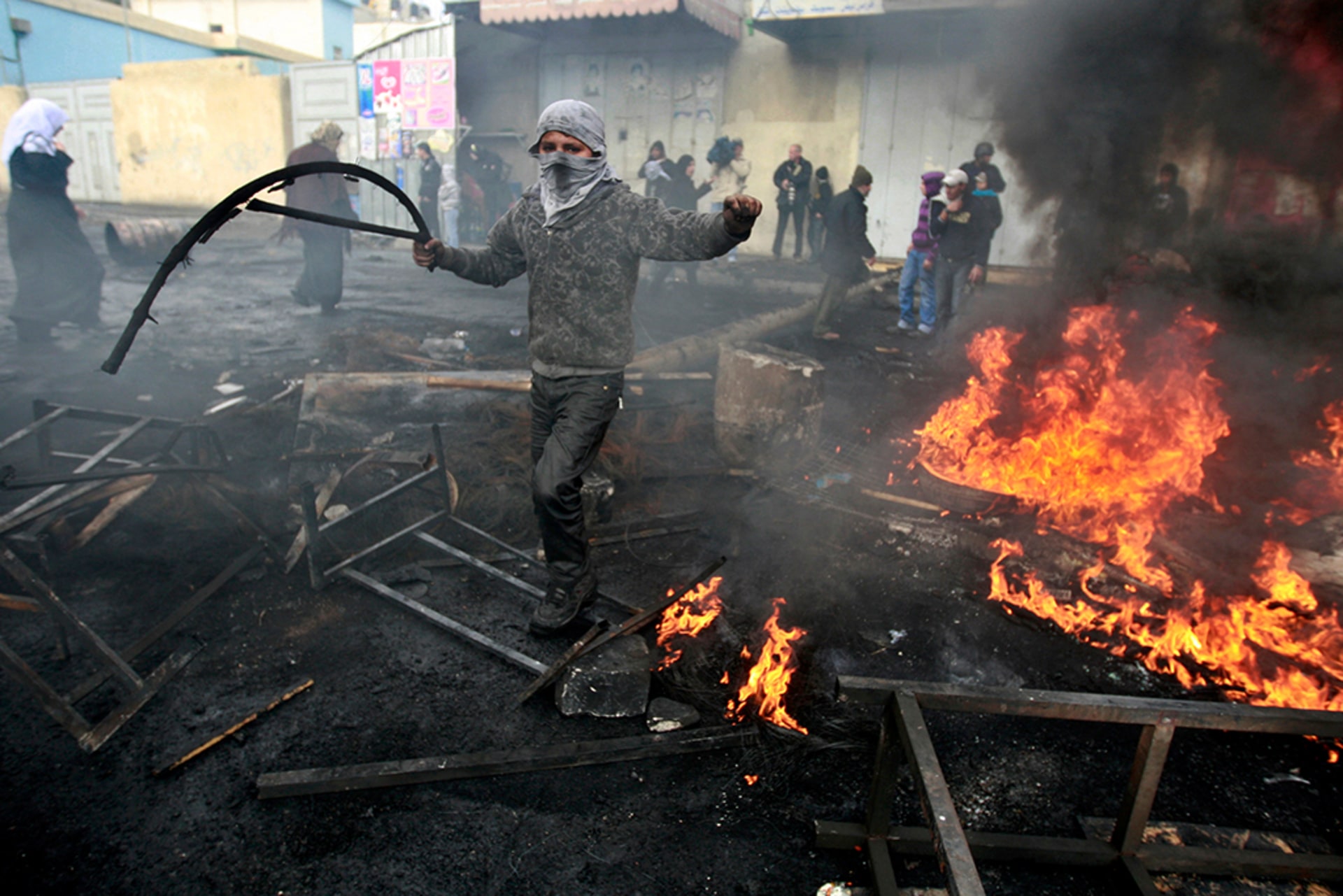 A Palestinian stone-thrower, protesting the Israeli offensive in Gaza, walks past tires set ablaze during scuffles with Israeli border police officers at Shuafat refugee camp in the West Bank. The protestor wears a protective facial covering.