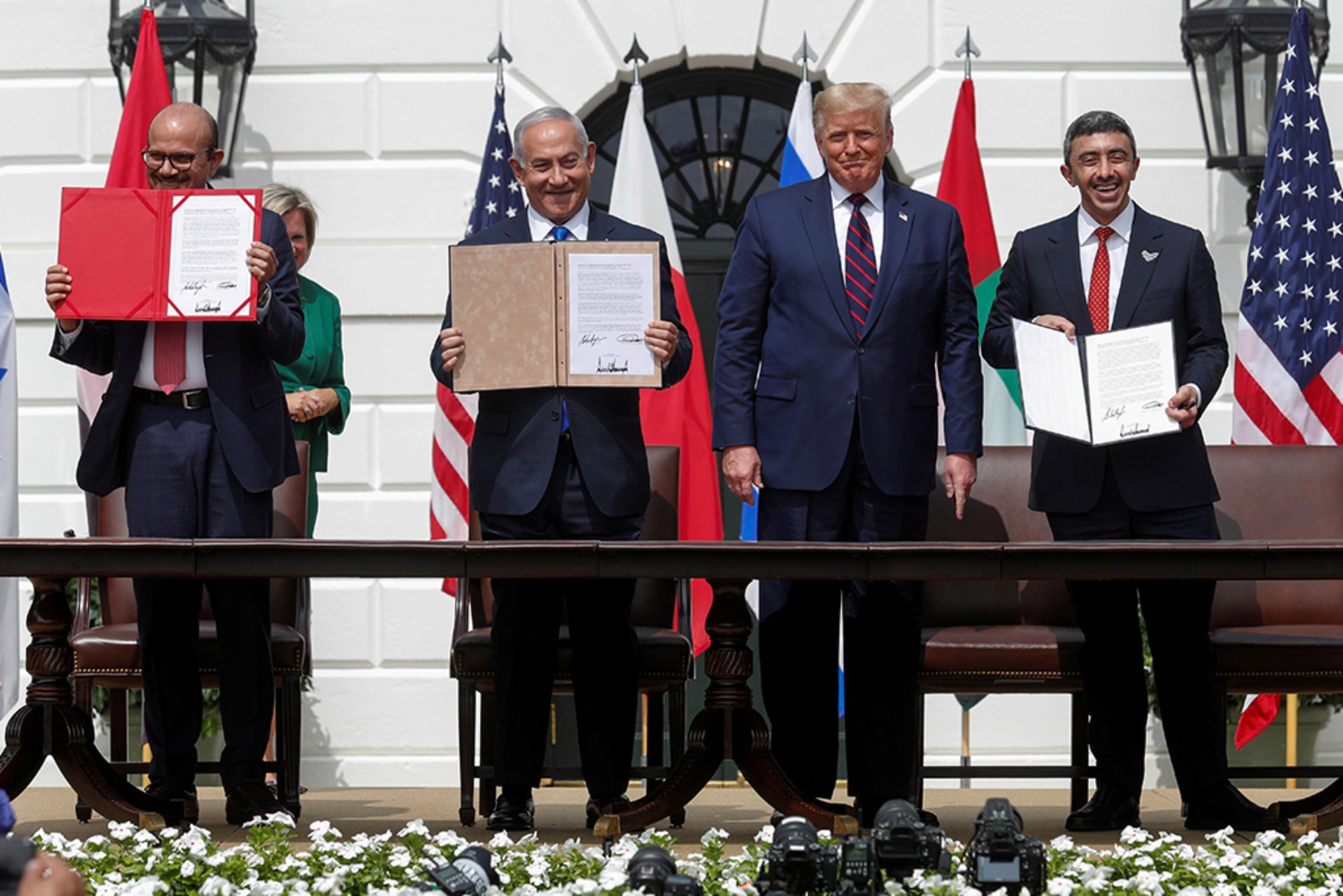 Bahrain's Foreign Minister Abdullatif Al Zayani, Israel's Prime Minister Benjamin Netanyahu, and United Arab Emirates (UAE) Foreign Minister Abdullah bin Zayed stand smiling as they display their copies of signed agreements. Former U.S. President Donald Trump stands between them.