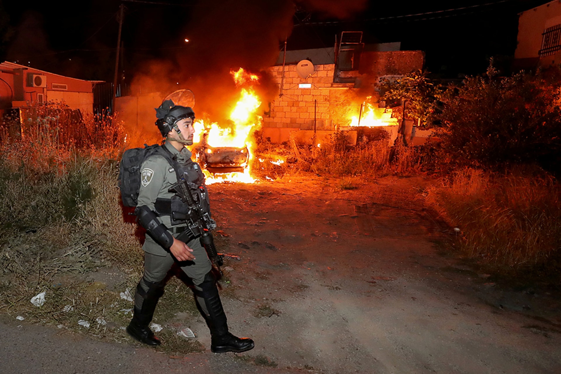 An Israeli border policeman walks in uniform as a car belonging to Jewish settlers burns amid tension over the possible eviction of several Palestinian families from homes on land claimed by Jewish settlers.