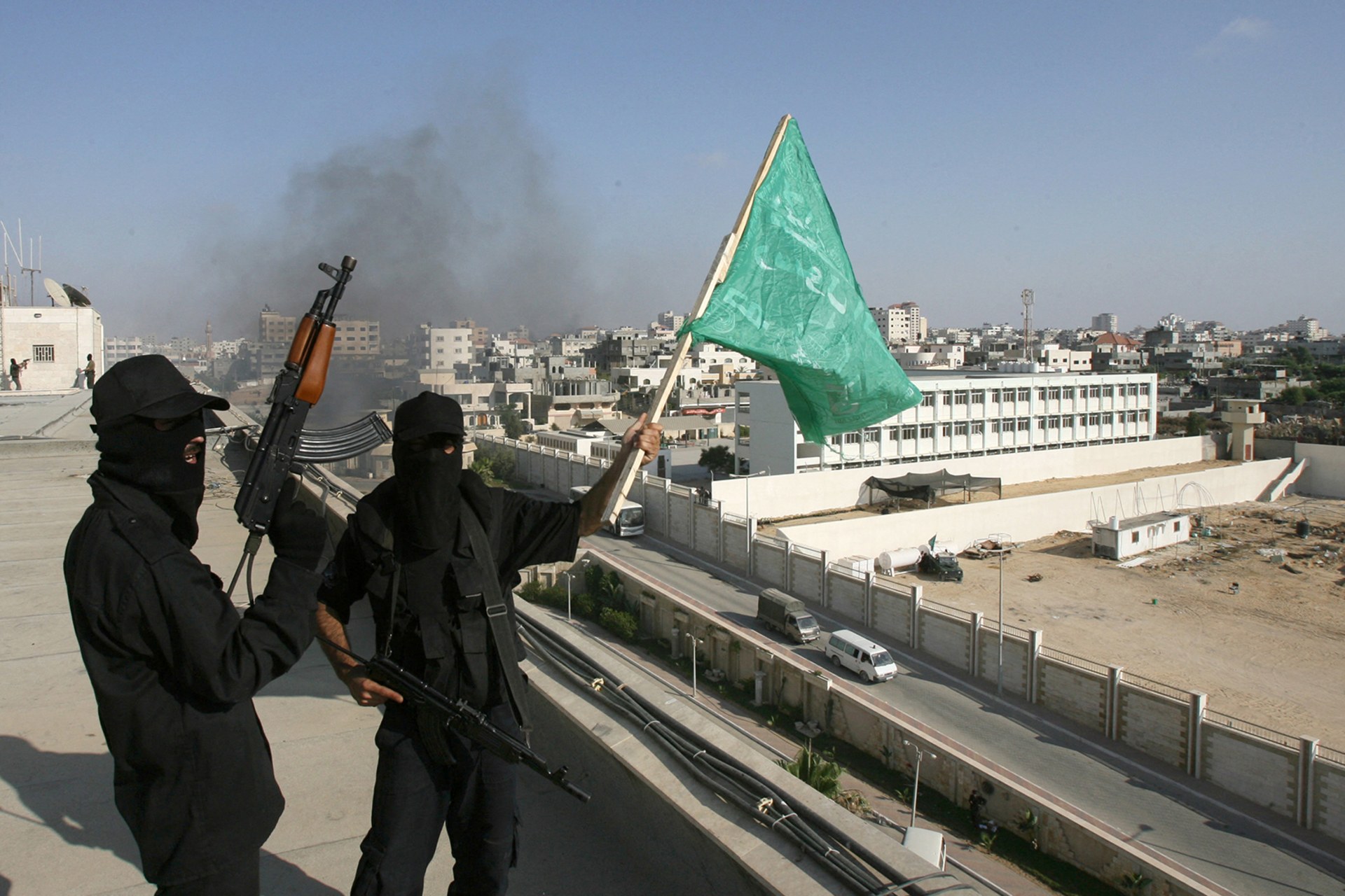 Hamas militants, dressed in all black and holding weapons, are seen on the roof top of the Palestinian Intelligence Security compound in Gaza City holding up the green Hamas flag.
