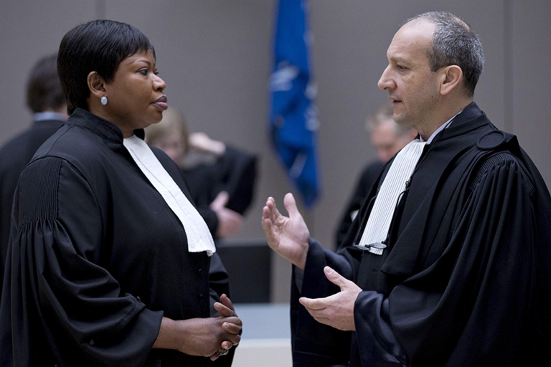 Two lawyers in proper attire converse with one another at the International Criminal Court.