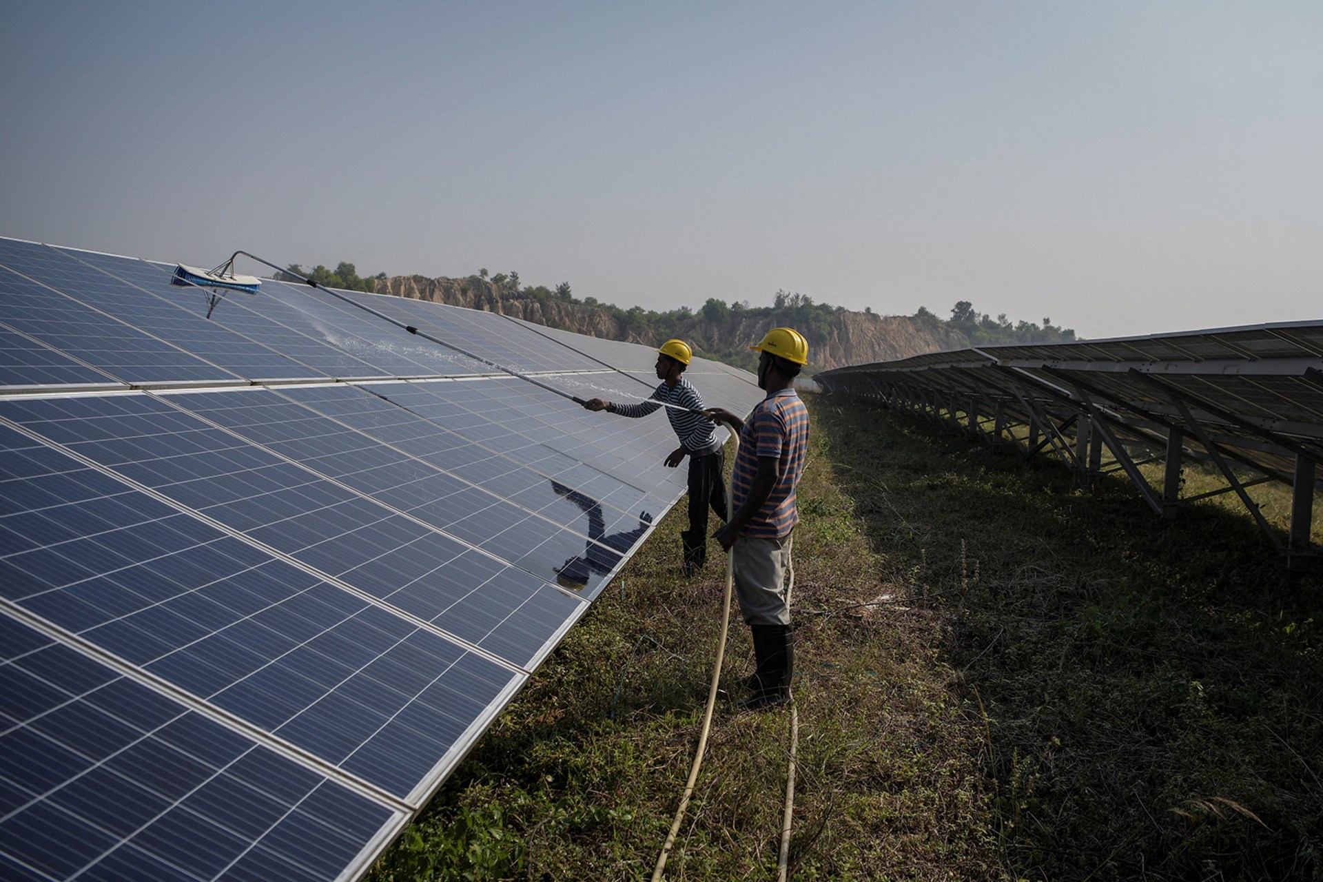 Two workers with cleaning equipment clean installed solar panels in a field.