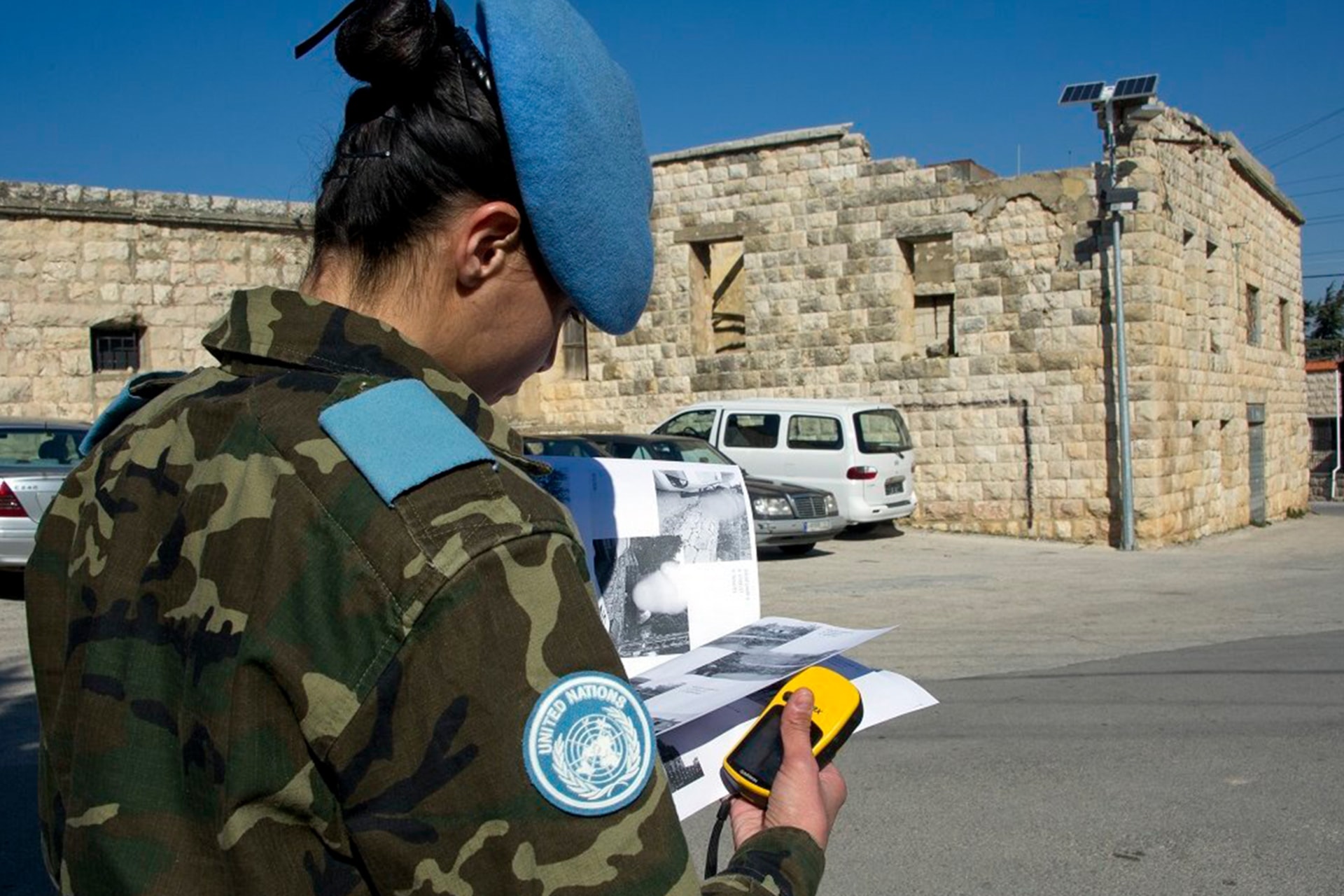 Photo of a UN Interim Force in Lebanon peacekeeper reading a paper, holding a device, and reviewing the installation of solar street lighting in Ibl al-Saqi.