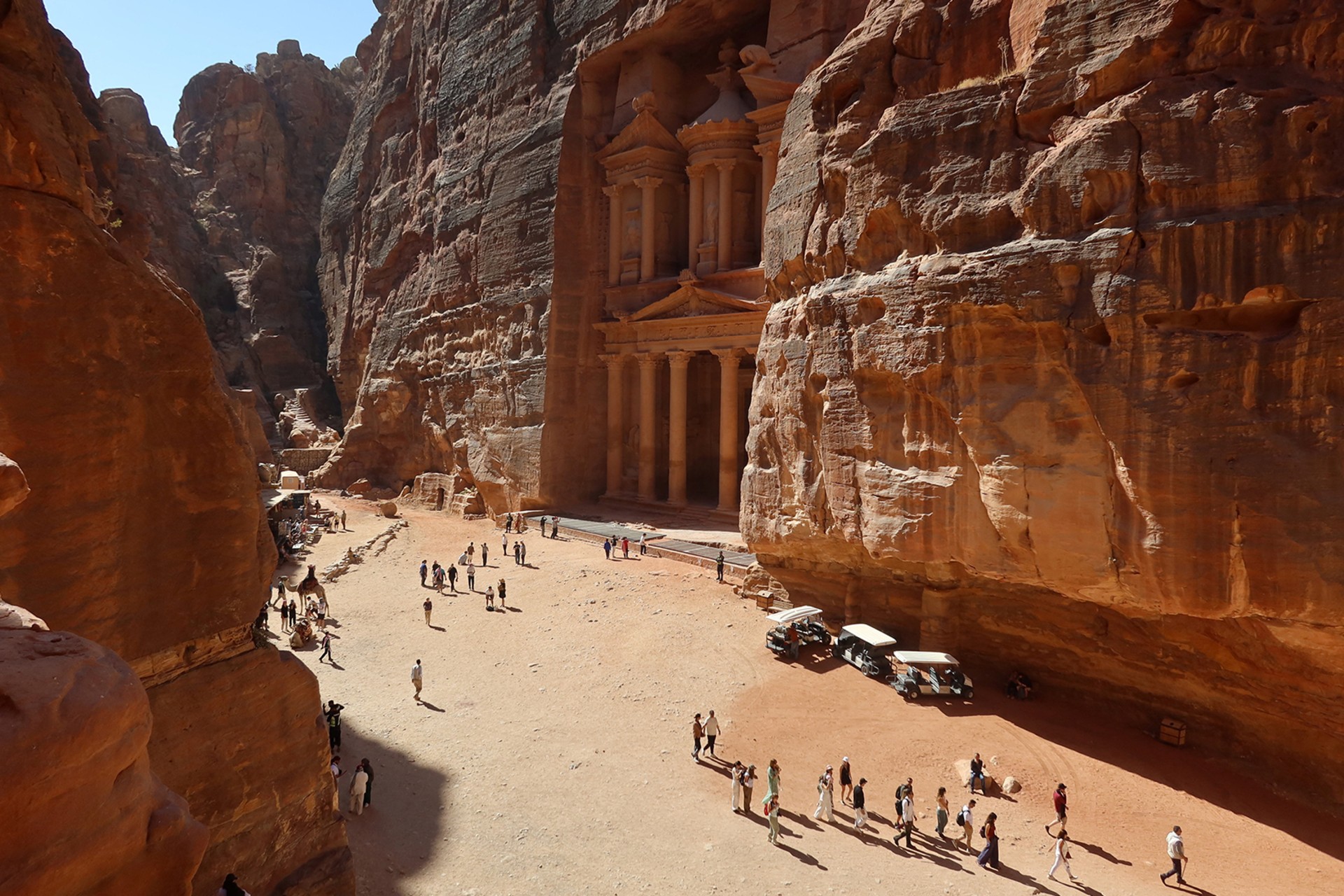 People walk in the ancient city of Petra, Jordan. There are rock structures and man made structures around them.