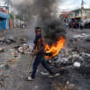 A young man walks past a burning barricade on a street.