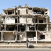 A man stands in front of a damaged building.