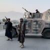 Taliban men holding guns next to a tank with mountains in the background.