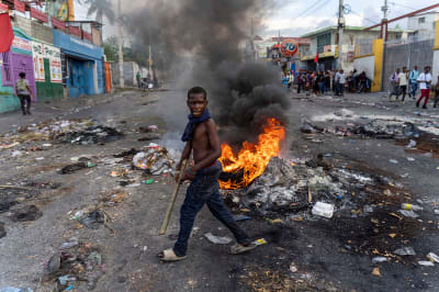 A young man walks past a burning barricade on a street.