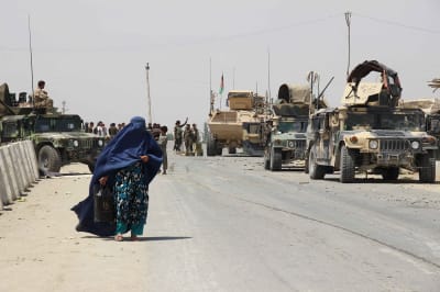 Woman in burqa walking next to tanks.