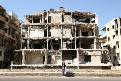A man stands in front of a damaged building.