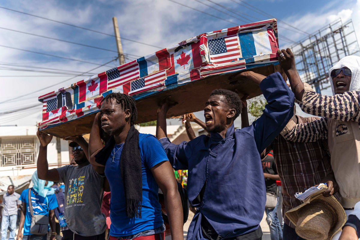 Four men hold a coffin draped in American, French, and Canadian flags over their head.