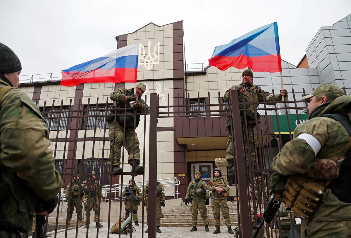 Servicemen of pro-Russian militia hoist flags of Russia and the separatist self-proclaimed Luhansk People’s Republic (LNR) outside a bank branch in Stanytsia Luhanska in the Luhansk region, Ukraine, on February 27, 2022. 