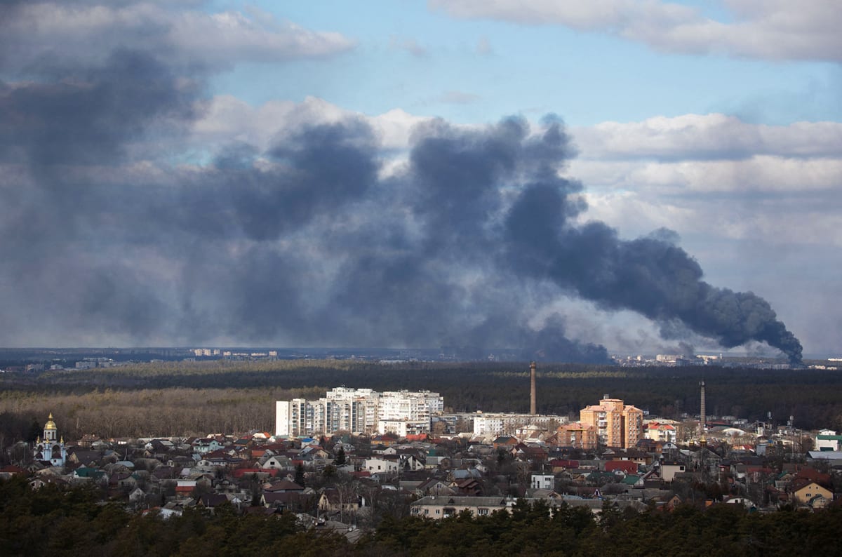 Smoke billows in a blue sky above one-story houses