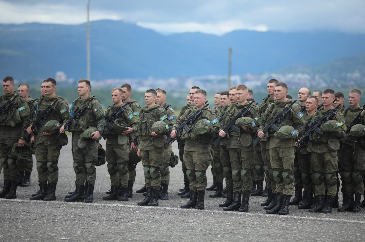 Soldiers stand at attention in front of mountains.