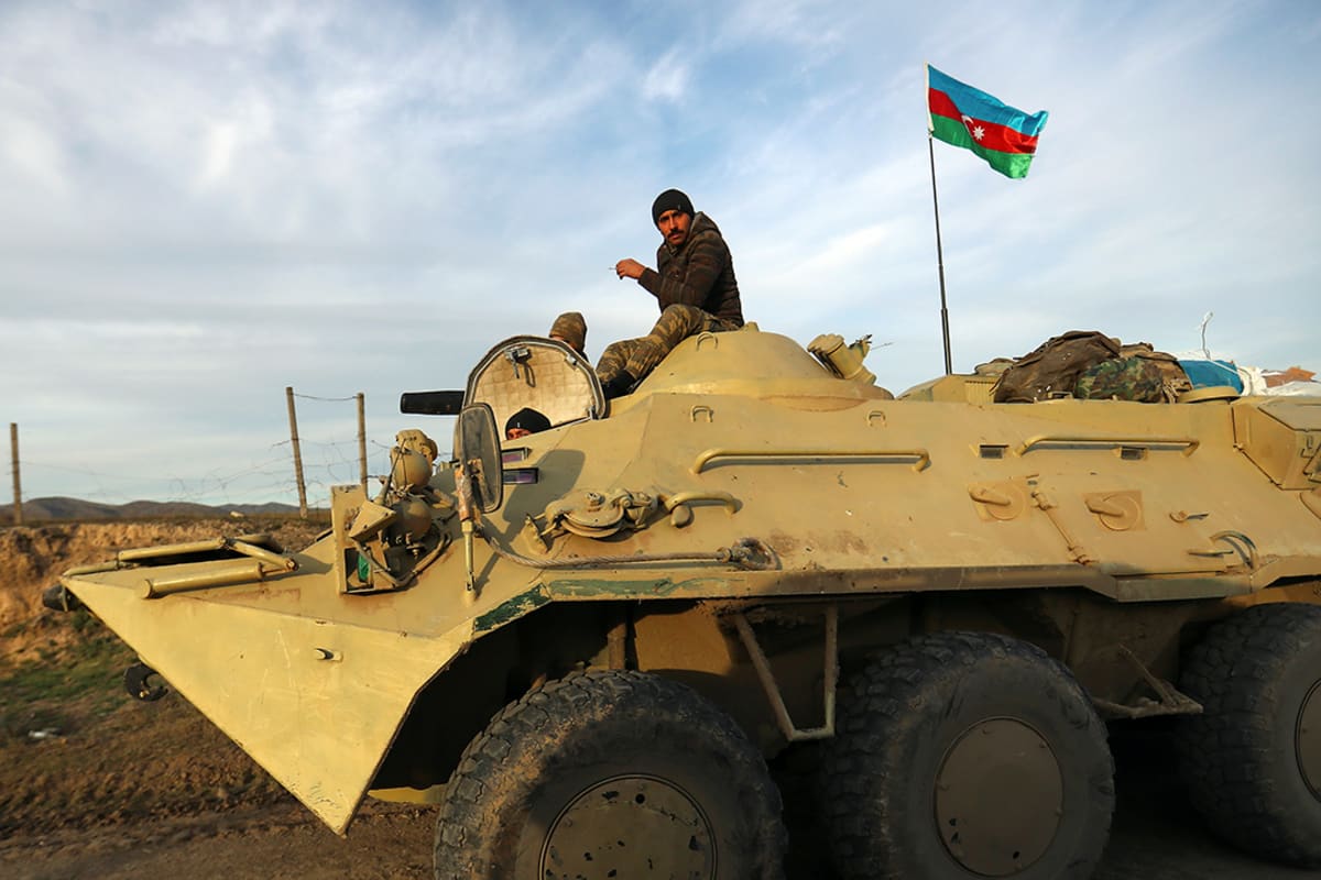A soldier sits on top of an armored vehicle.