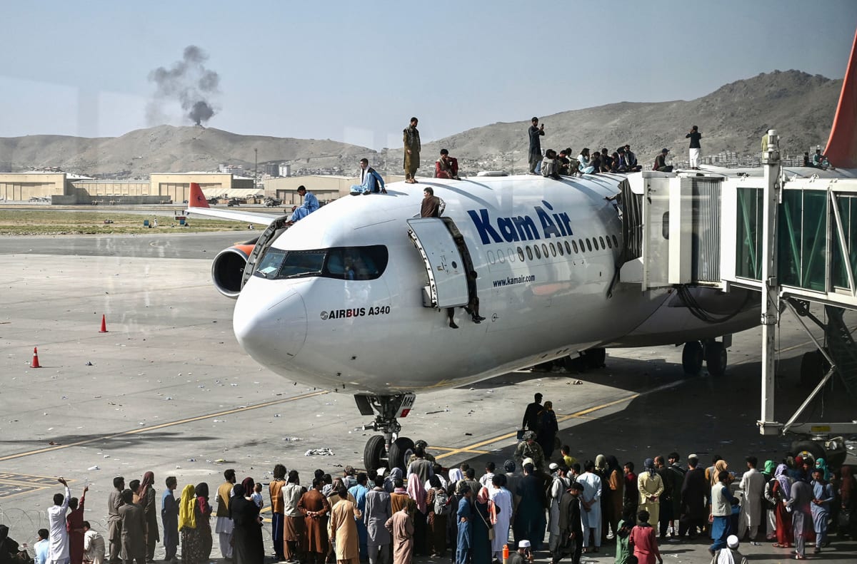Afghan people climb atop a plane as they wait at the Kabul airport in Kabul on August 16, 2021.