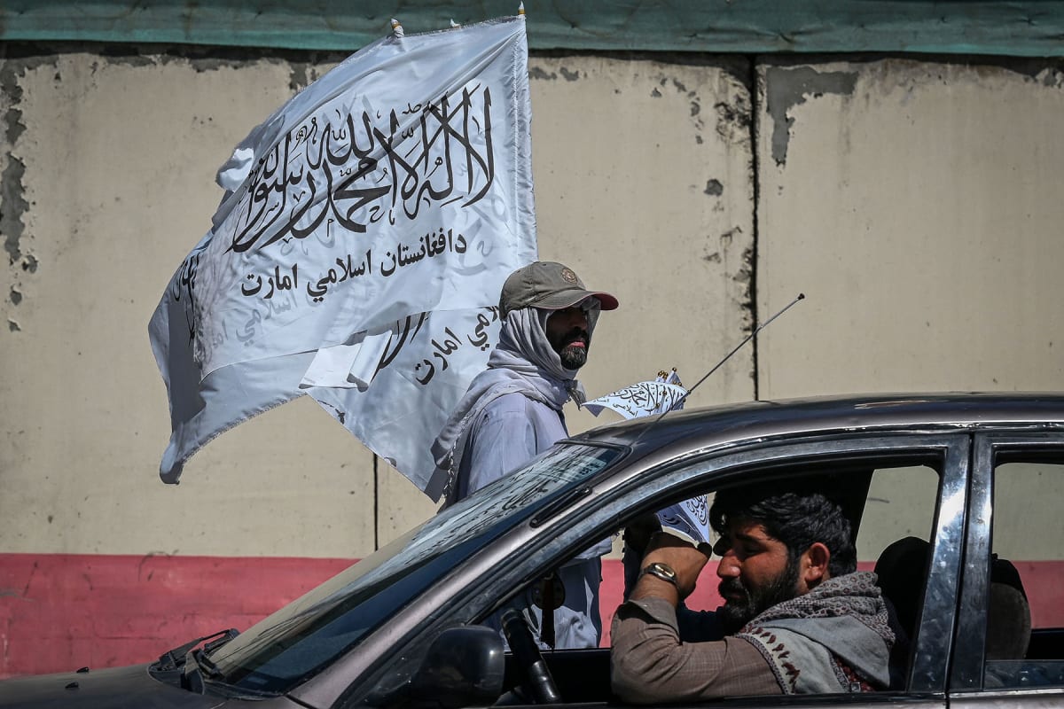 A mobile hawker carries Taliban flags as commuters make their way along a road in Kabul on September 5, 2021.