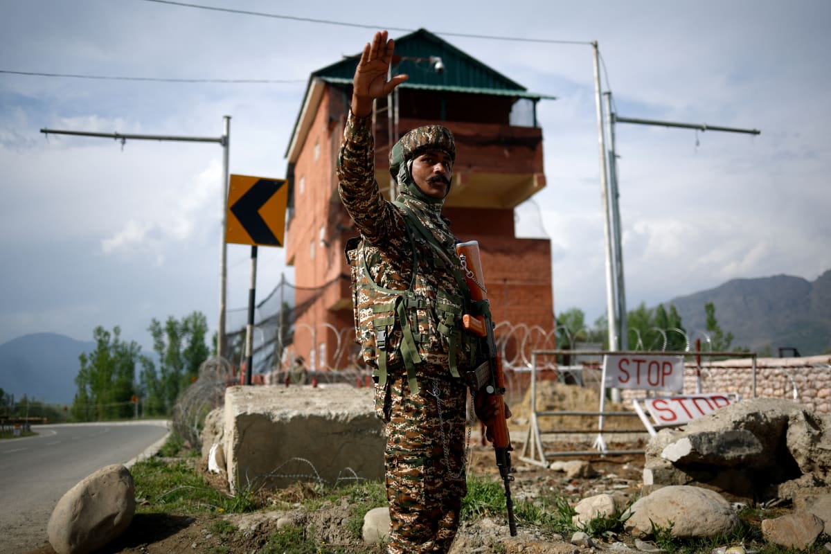 An Indian soldier raises his right arm up while holding a gun in the other at a border crossing in the mountains.