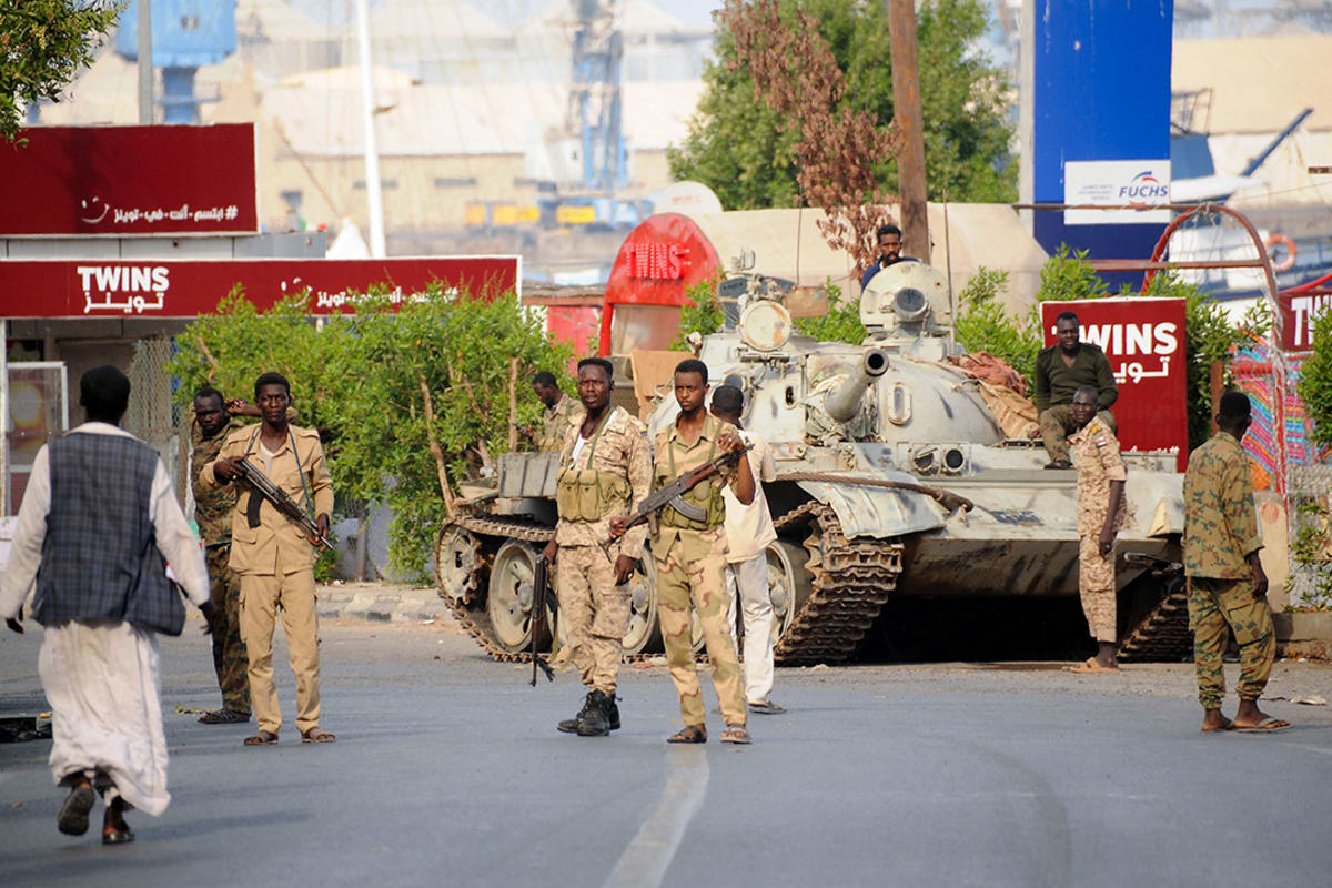 Soldiers stand guard in front of a military tank.
