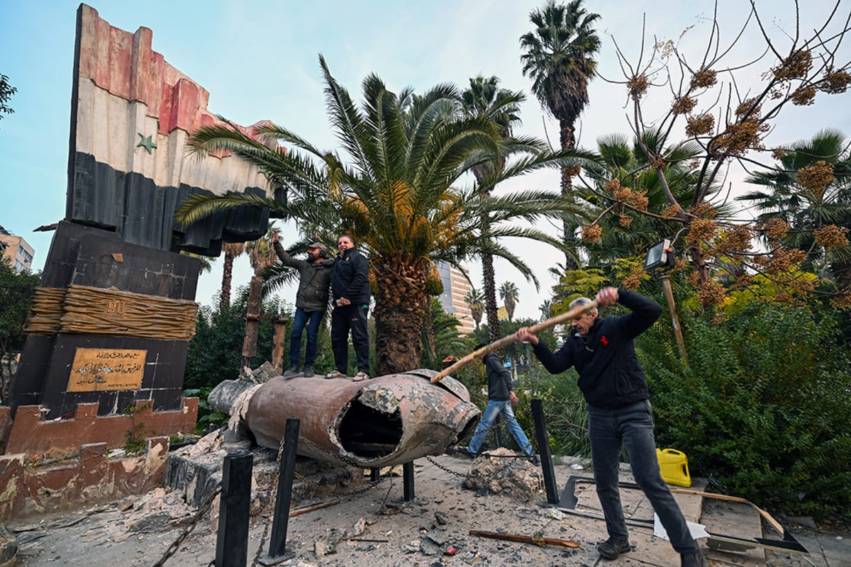 People stand outside a building next to a toppled statue.