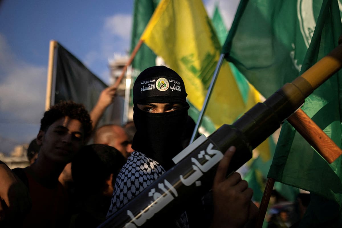 A young person wears black clothing and a black balaclava holding green and yellow flags