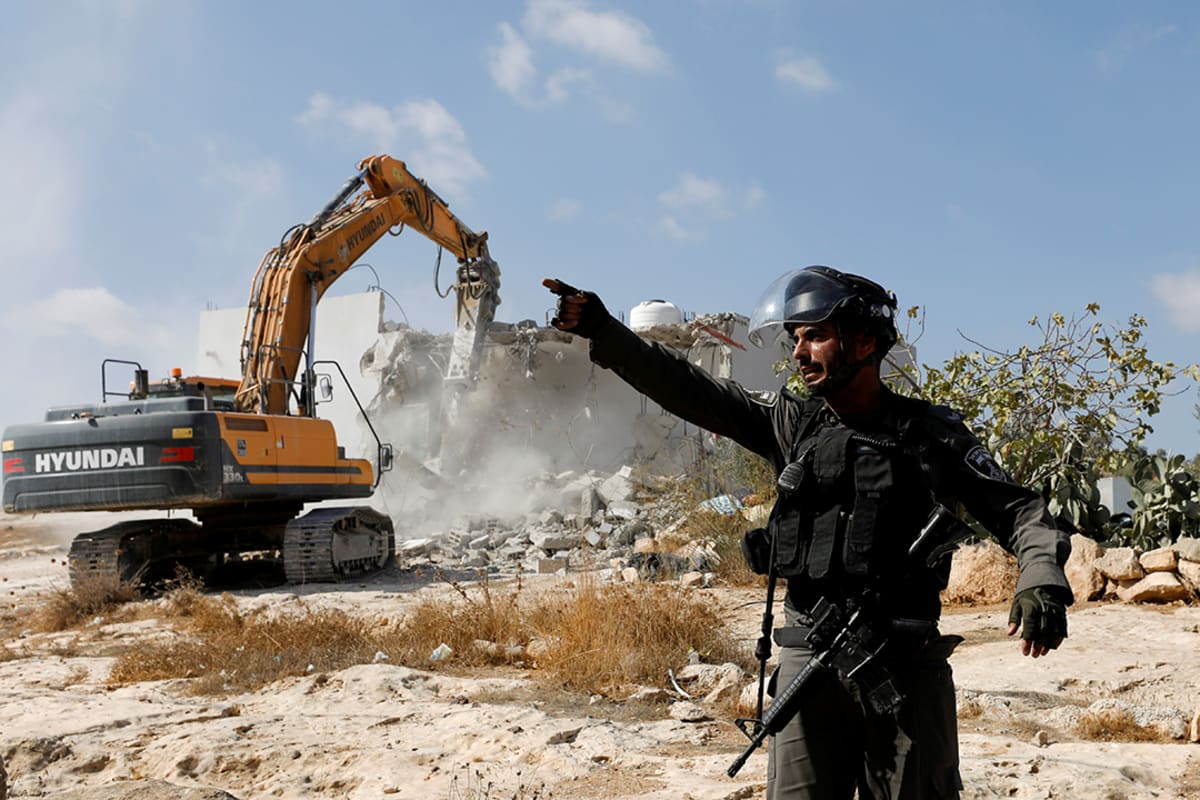 An Israeli border police officer gestures as machinery demolishes a Palestinian house near Yatta, in the West Bank, on November 3, 2021.
