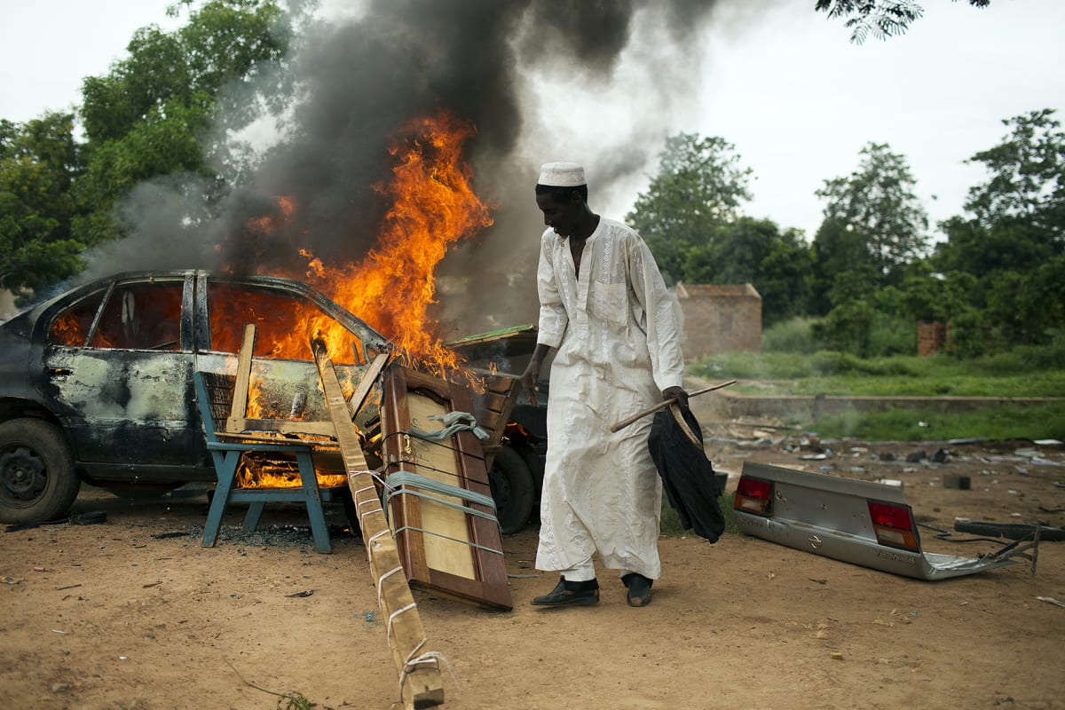 A man stands near a vehicle and other belongings set on fire by its owners who did not want to leave them behind for looters as Muslim families prepare to be evacuated by road, with the held of an armed convoy escorted by African Union peacekeepers, near the PK12 neighborhood in Bangui, Central African Republic on April 27, 2014. 