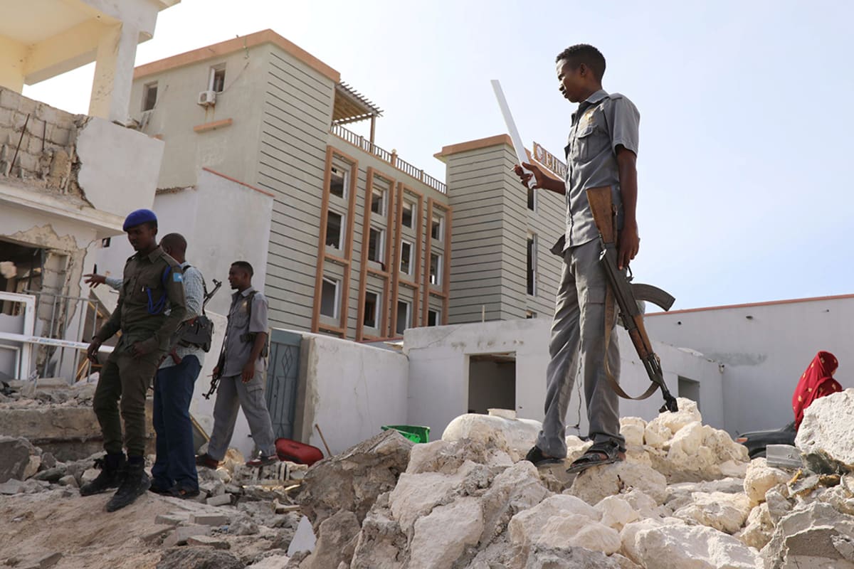 A man stands on a pile of rubble amid white damaged buildings.